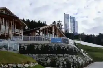 Moderne Außenansicht des Restaurants kAlps mit Holzarchitektur, Glasgeländern, Steinmauern und Berglandschaft im Hintergrund.