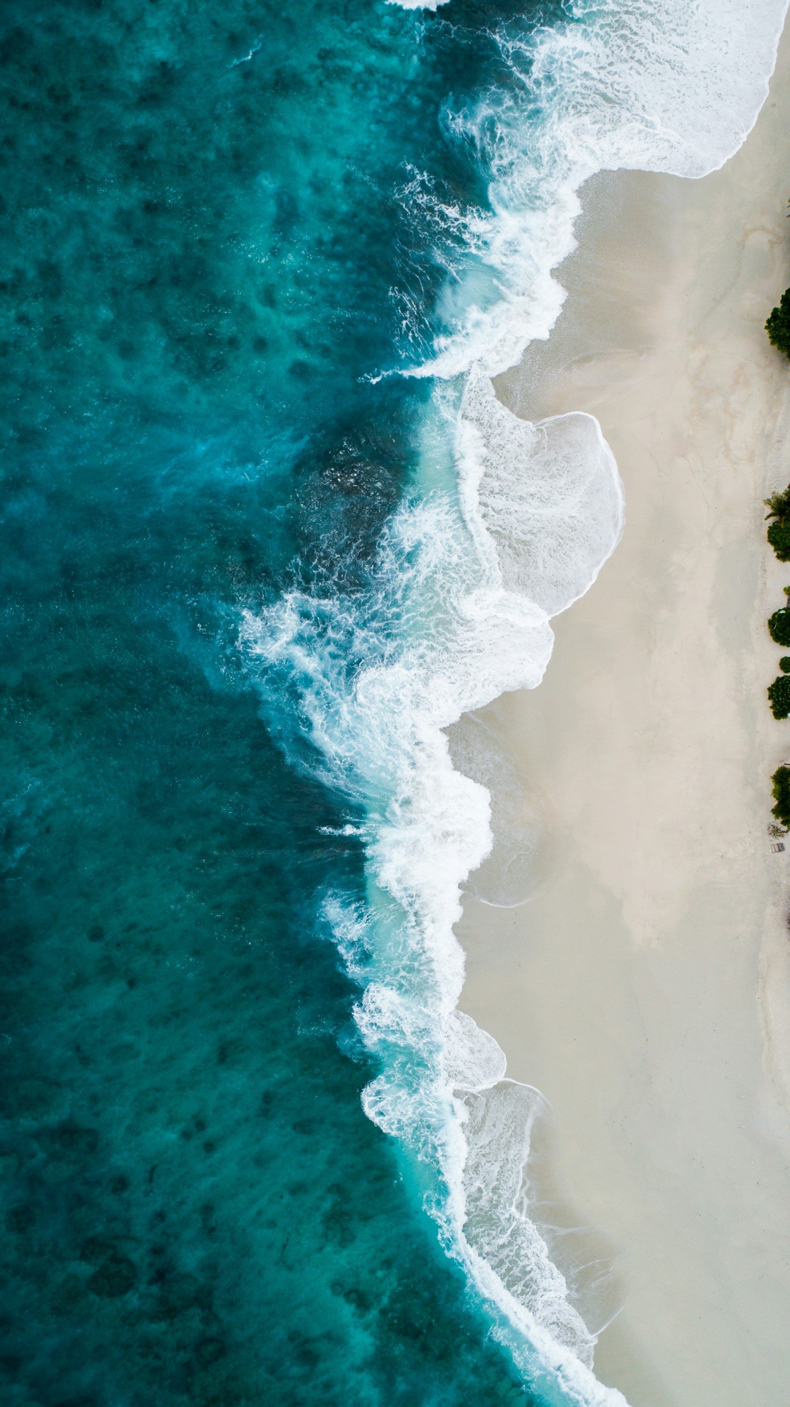 Aerial view of turquoise ocean water meeting a white sand beach in Southern California