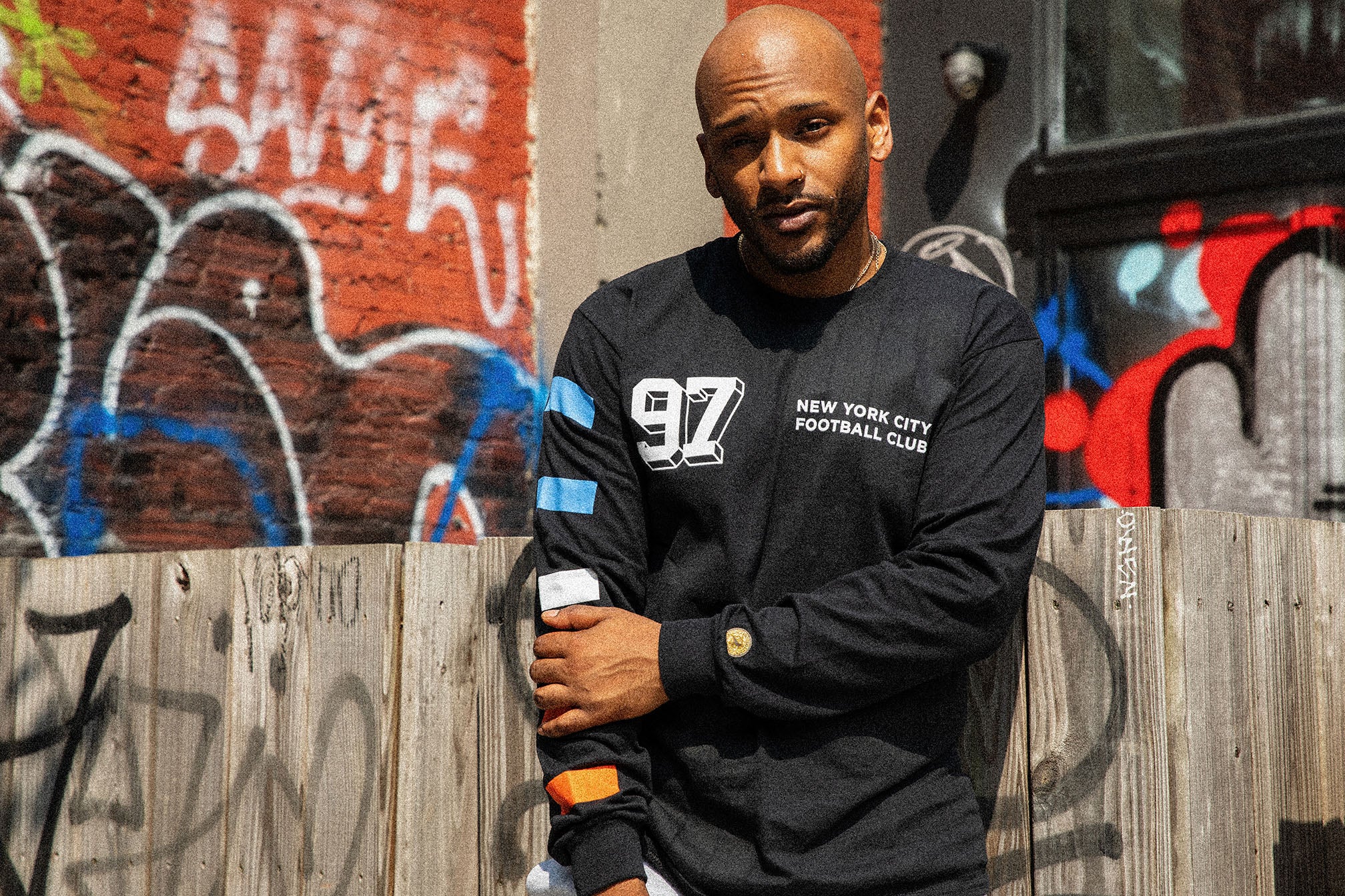 Portrait of model in a black NYCFC long sleeve in front of a graffiti-covered wall, photographed on the street in NYC.