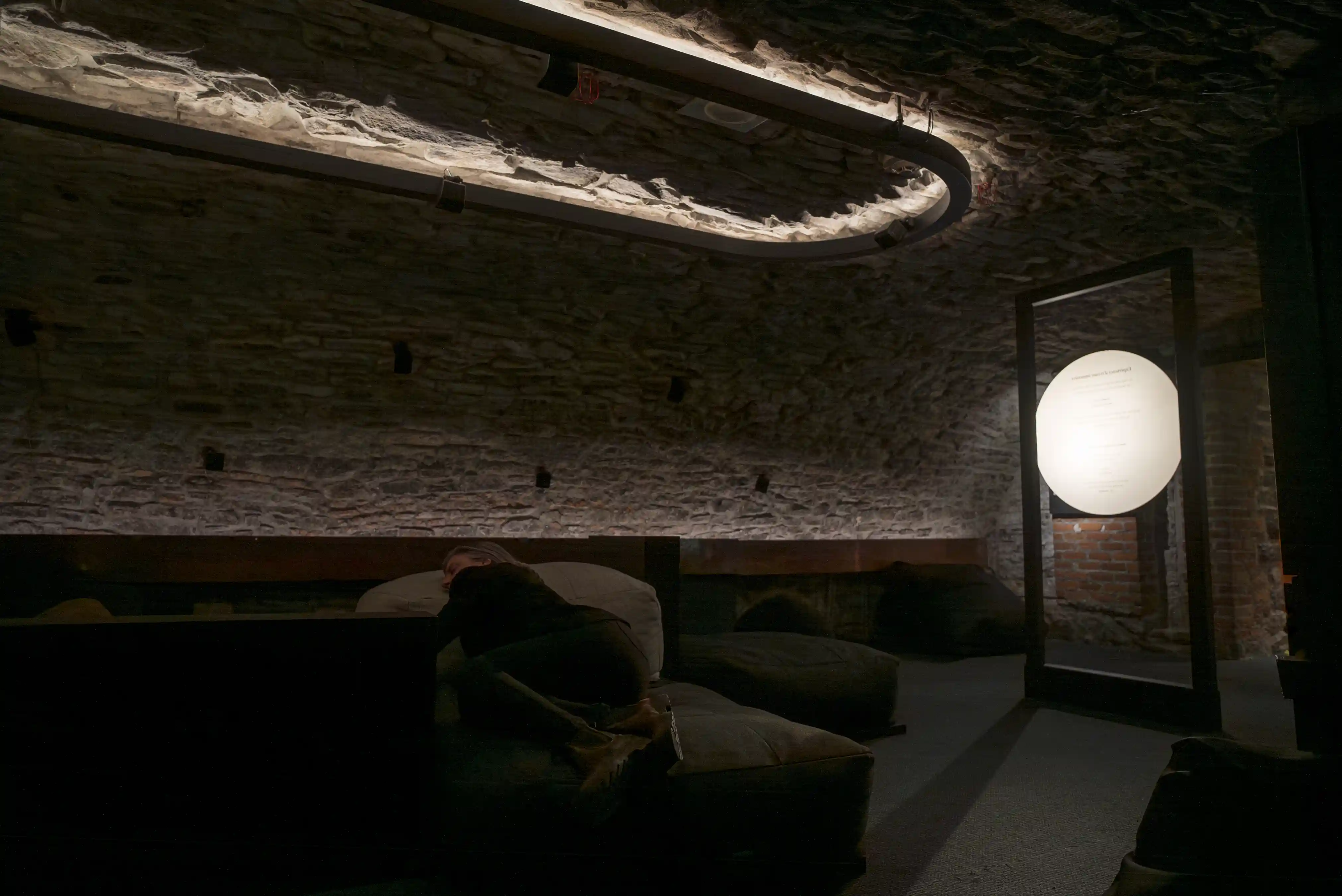 Salle voûtée en pierre avec installation lumineuse circulaire au plafond et un grand disque lumineux au sol, créant un espace d’écoute immersif.