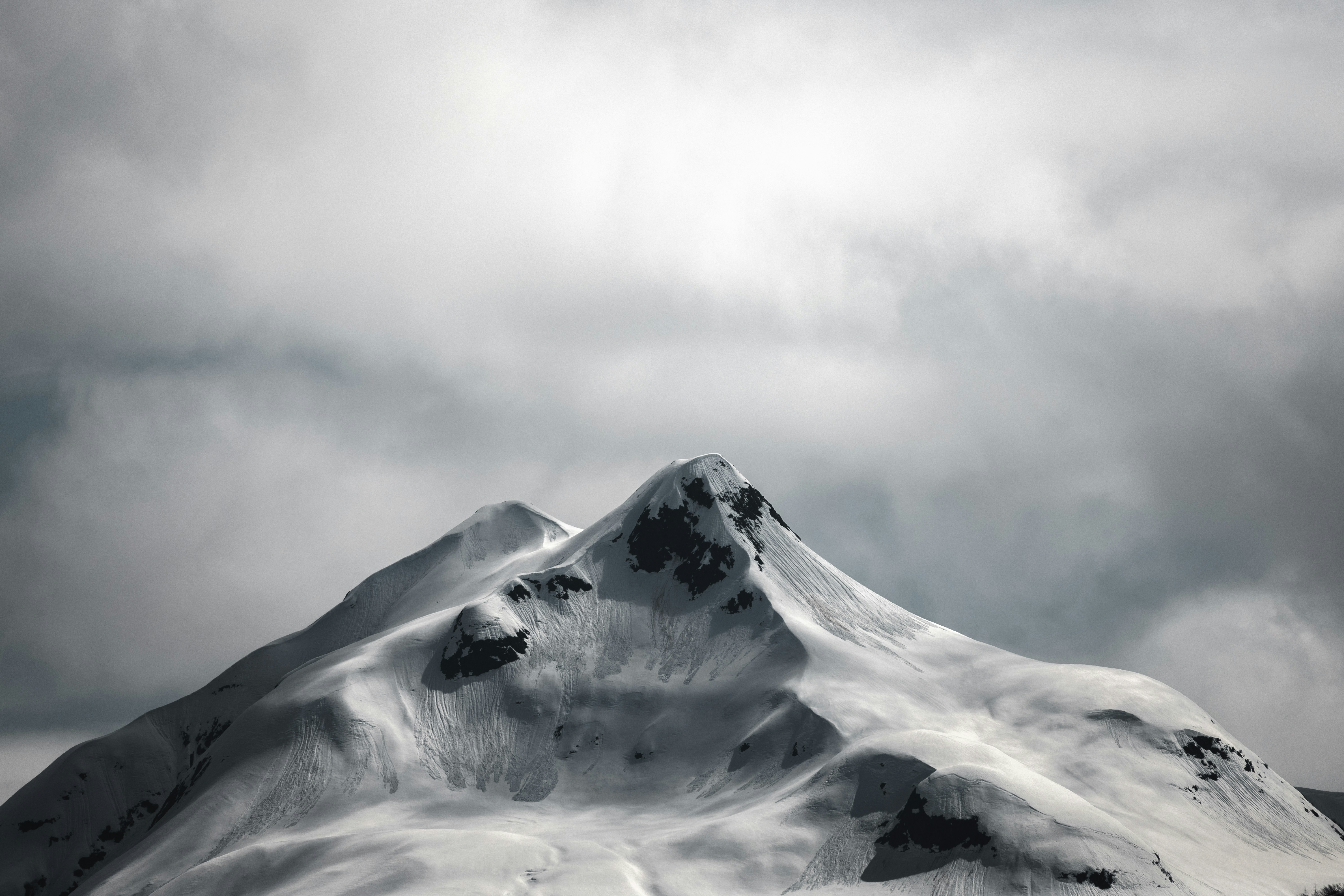 A snow-covered mountain peak under a dramatic cloudy sky.