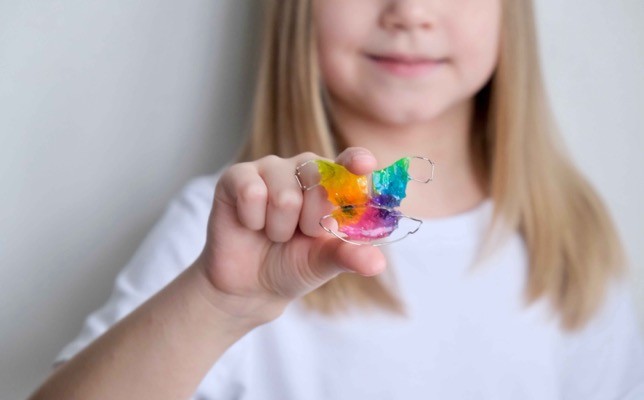 Barn viser frem en fargerik avtakbar tannreguleringsplate i hånden.