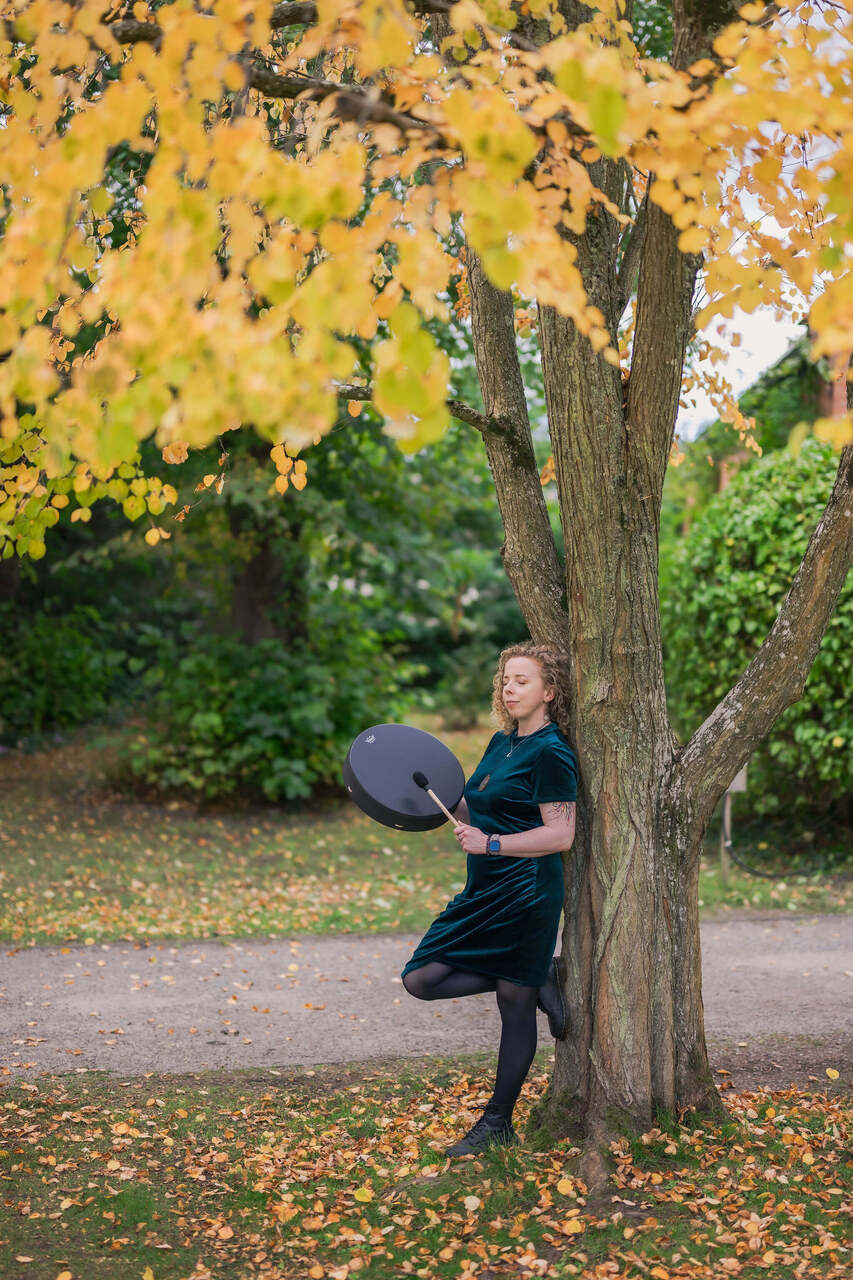 Maryrose leaning against a tree playing the drum
