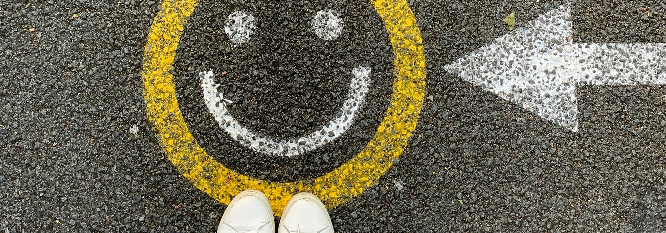 Yellow smiley face and arrow painted on pavement, symbolizing creativity, clarity, and positive brand direction.