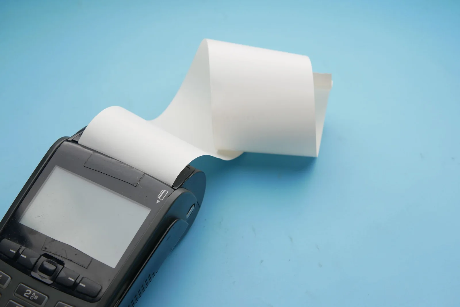 A payment terminal prints a blank receipt beside a roll of thermal paper.