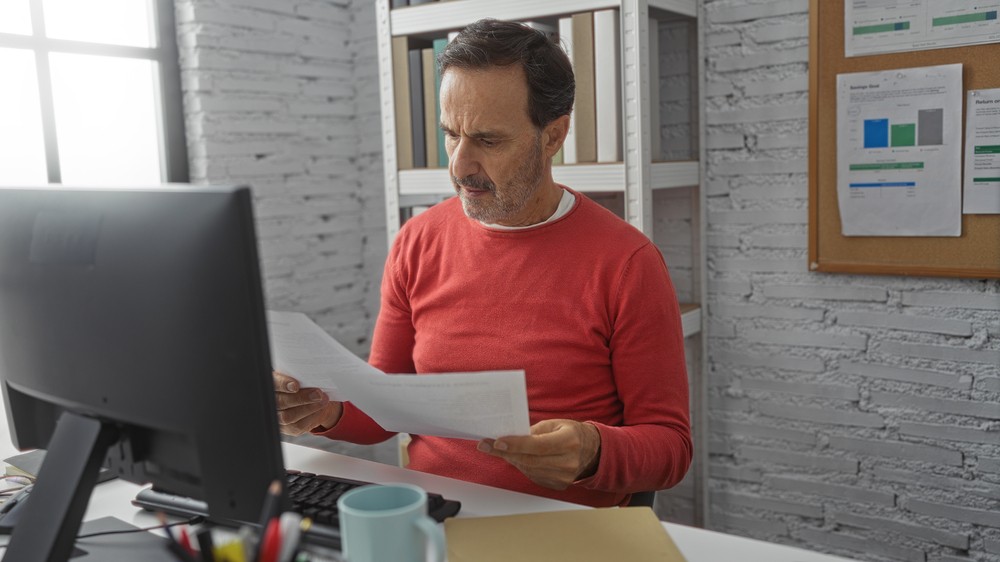 Homme examinant des documents à son bureau, symbolisant l'analyse des options entre assurance vie temporaire et permanente.