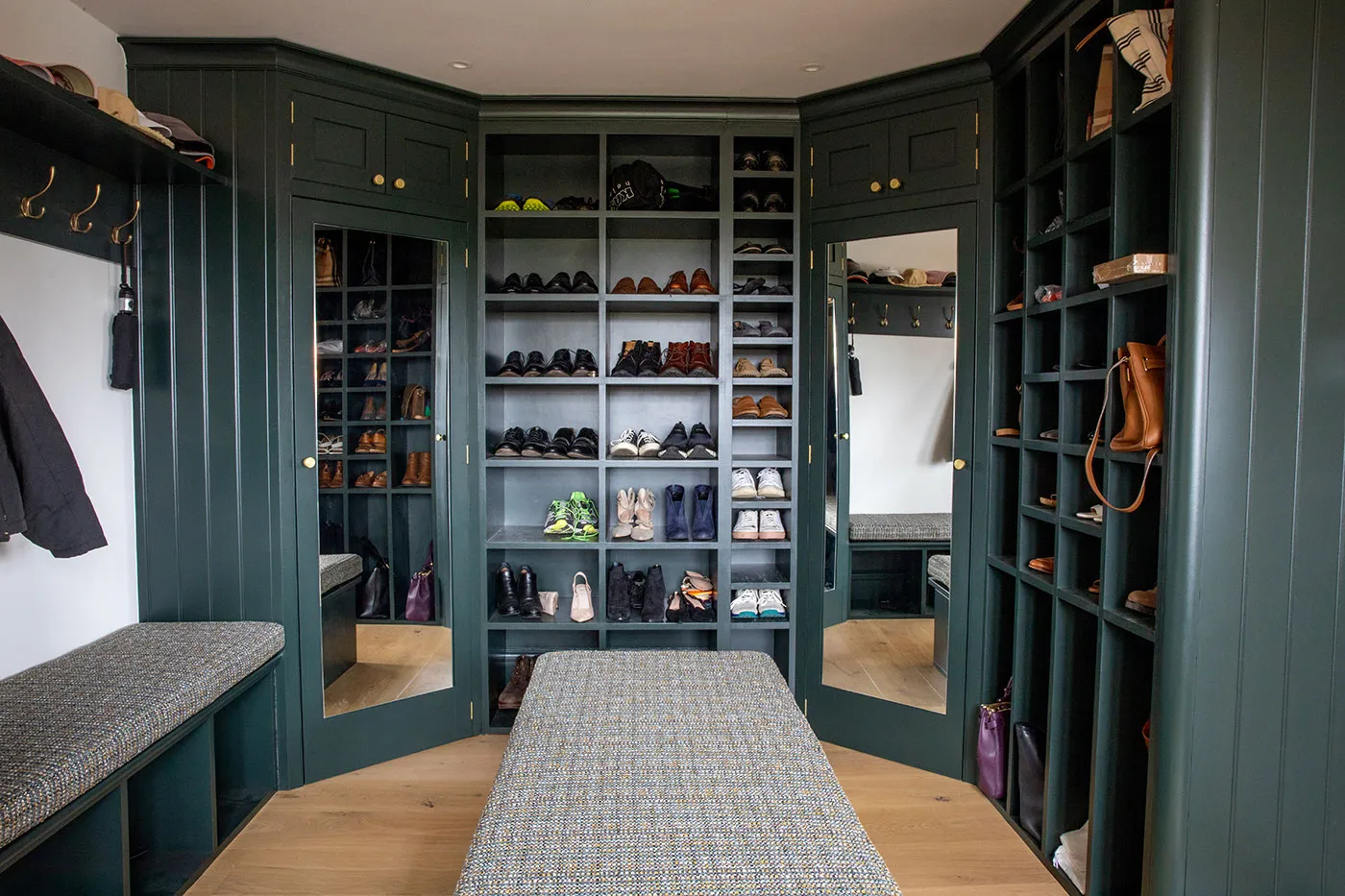 Walk-in closet with dark green shelving units and shoe storage with a bench in front of the shoe storage.
