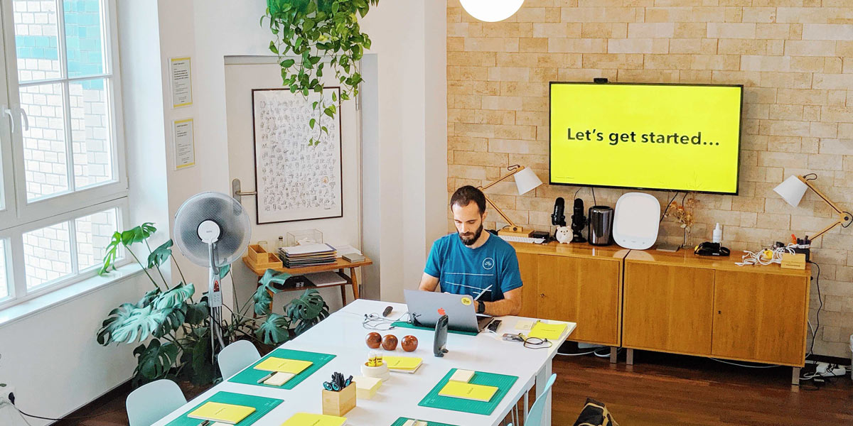 A workshop facilitator setting up for a remote workshop while sitting a front of his computer in a bright conference room. 