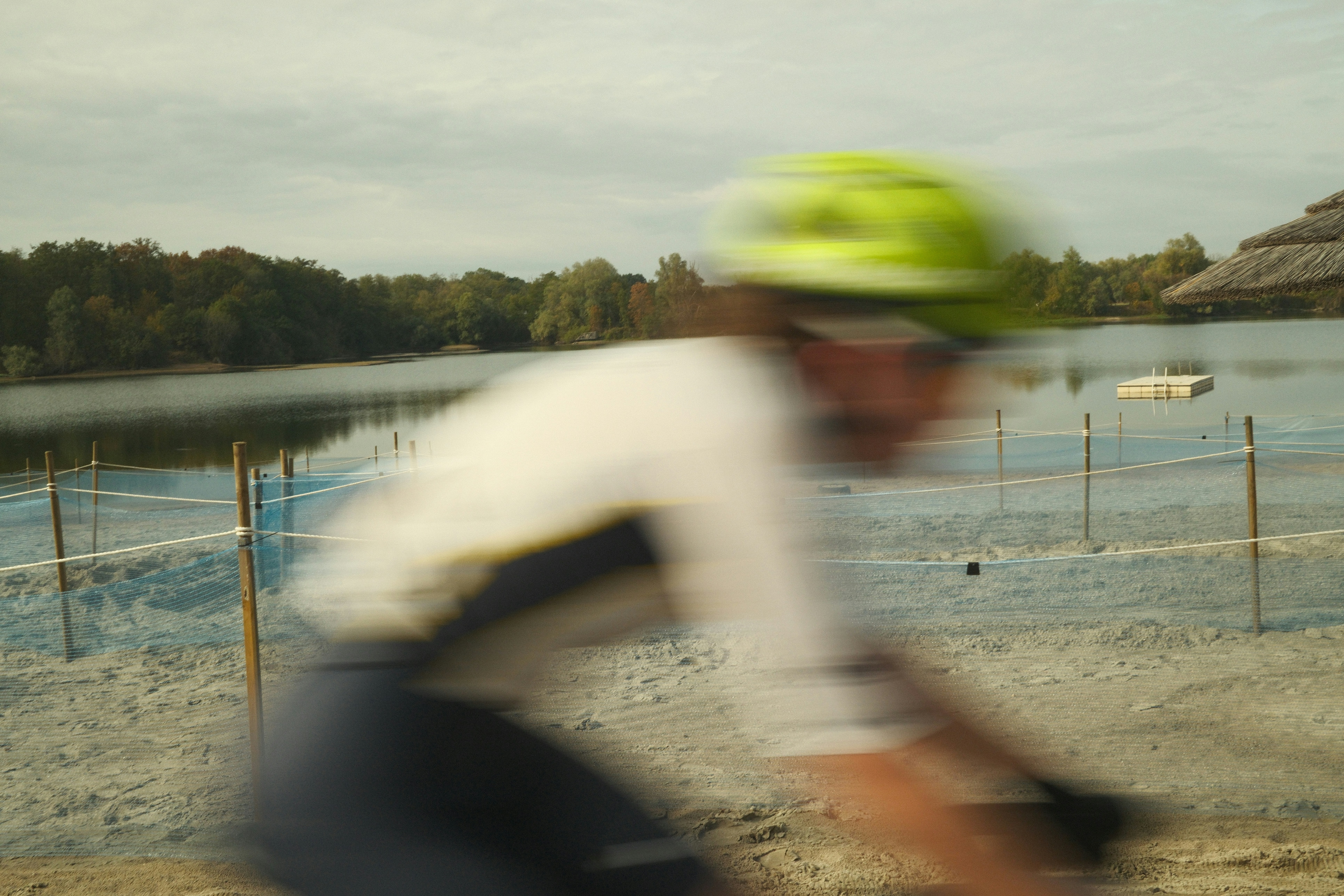 Motion blur photo of a cyclist in a bright green helmet riding past a lake
