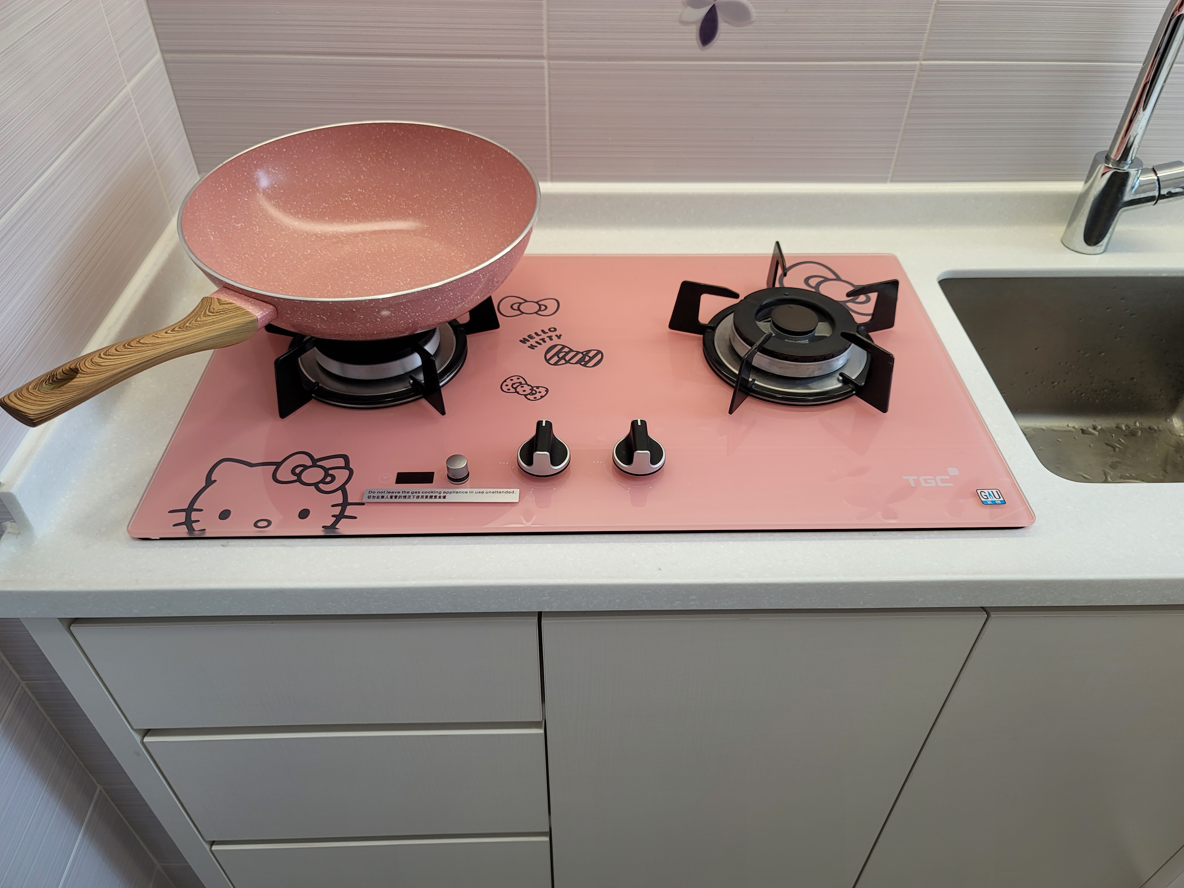 Pink glass-top gas stove with cartoon motifs as part of a quirky kitchen design on a white counter in Hoi Tat Estate.