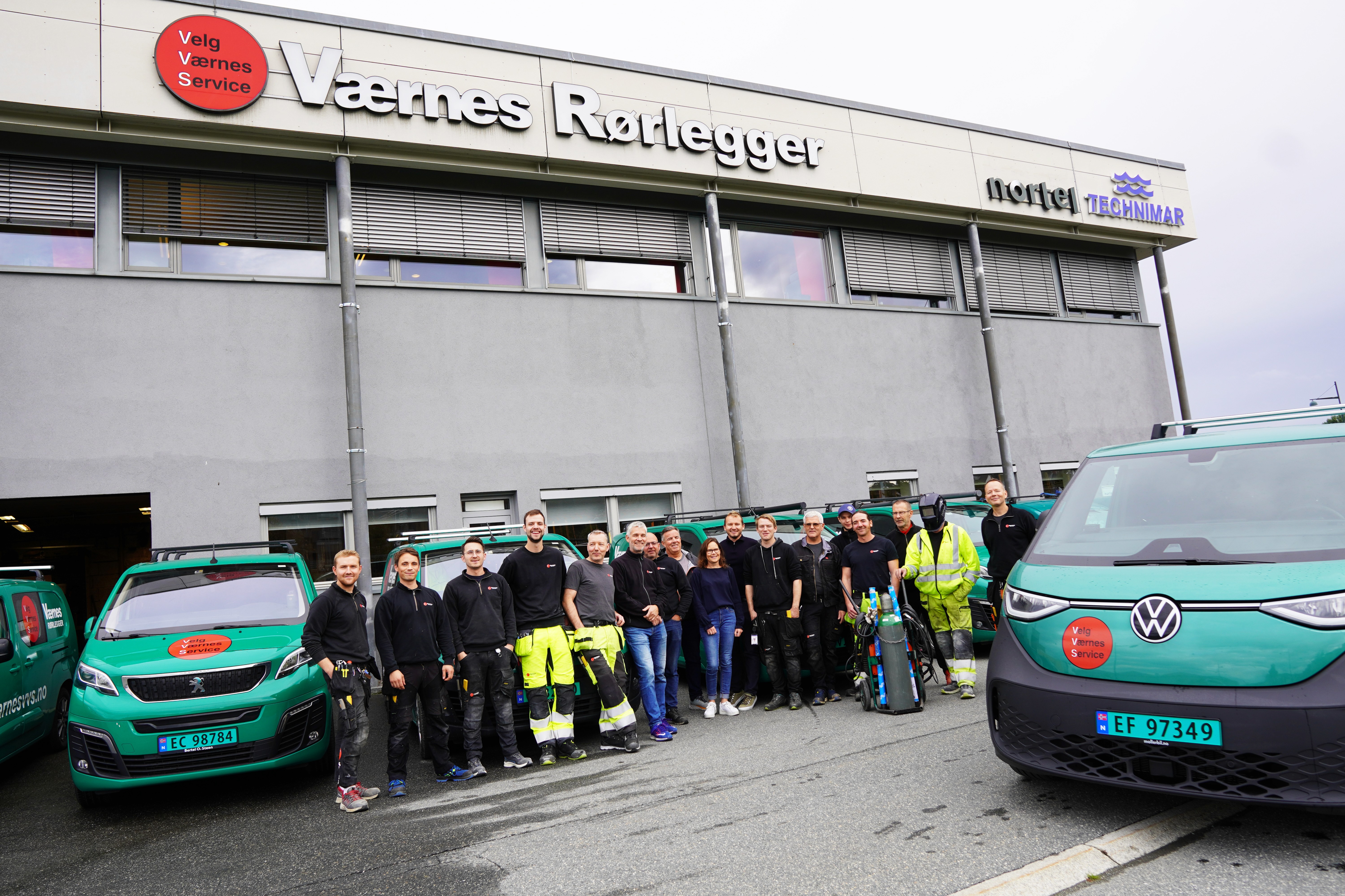 Ansatte i Værnes VVS foran kontorbygningen med grønne servicebiler på vær side