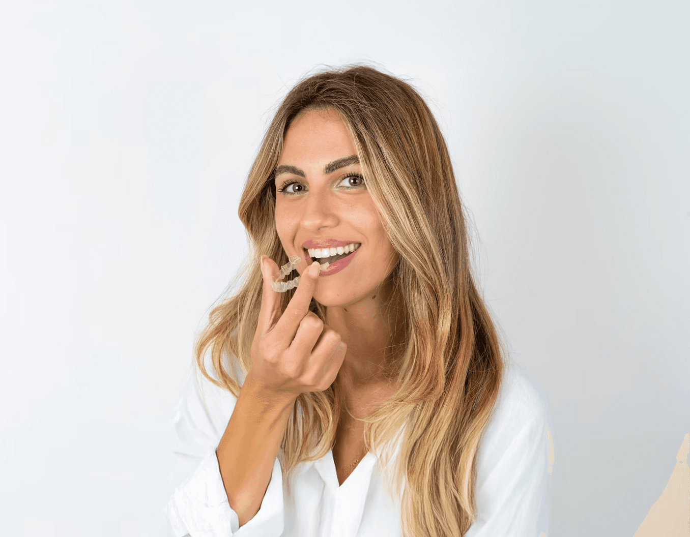 A woman smiles and holds invisalign clear aligners with a case, showcasing a certified invisalign provider at Bella Medical Centre