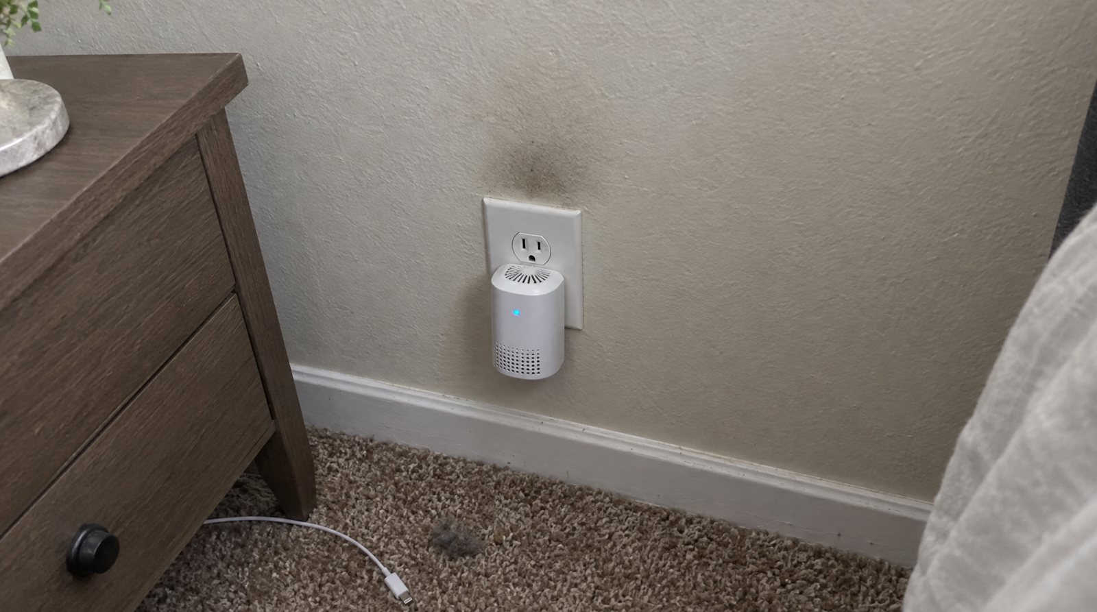 A faint grey shadow on white wall paint just above a plug-in purifier in an outlet.