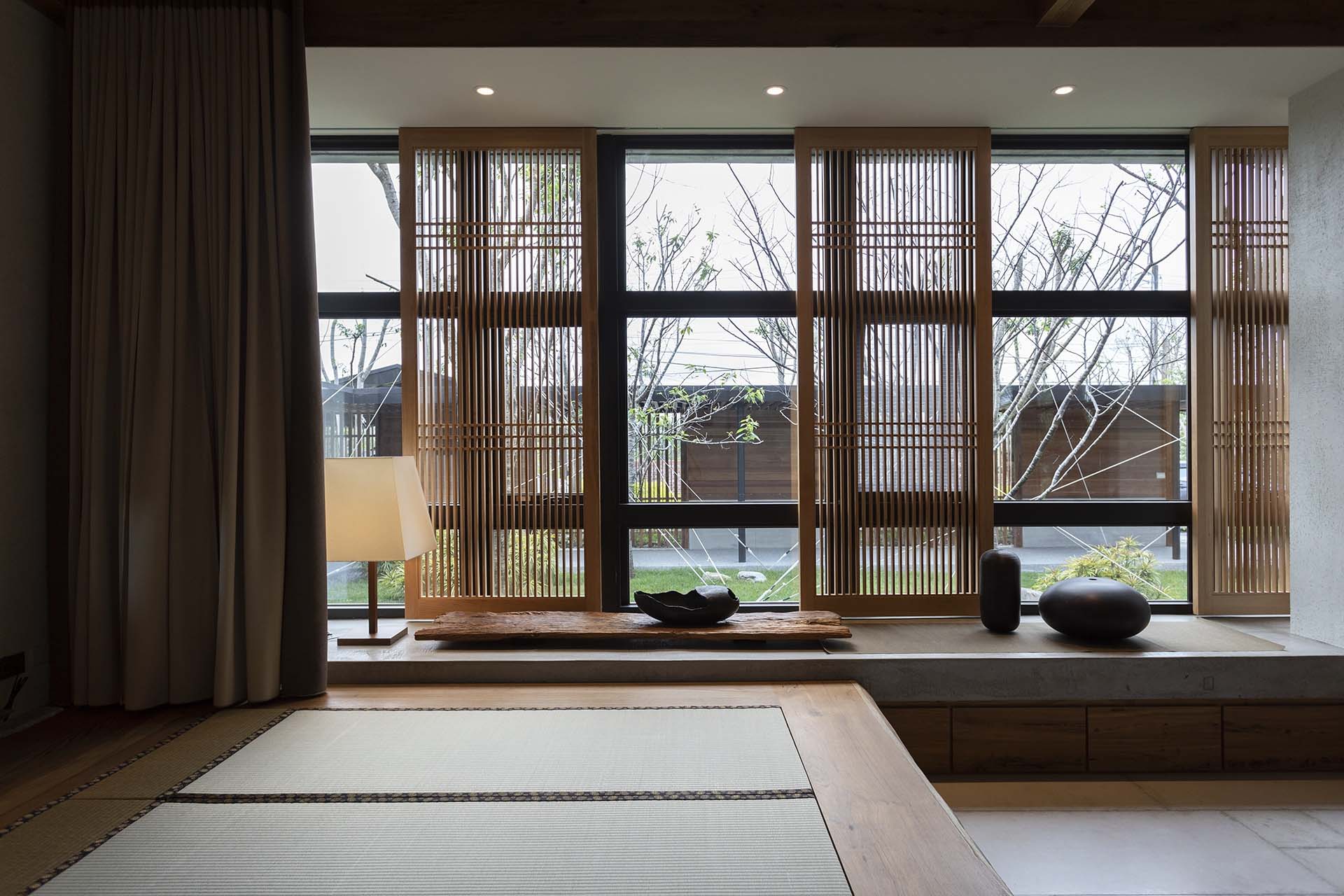 榻榻米開方式臥榻、細木格柵與大面窗景，窗台擺放陶器與木雕，呈現日式寧靜之美