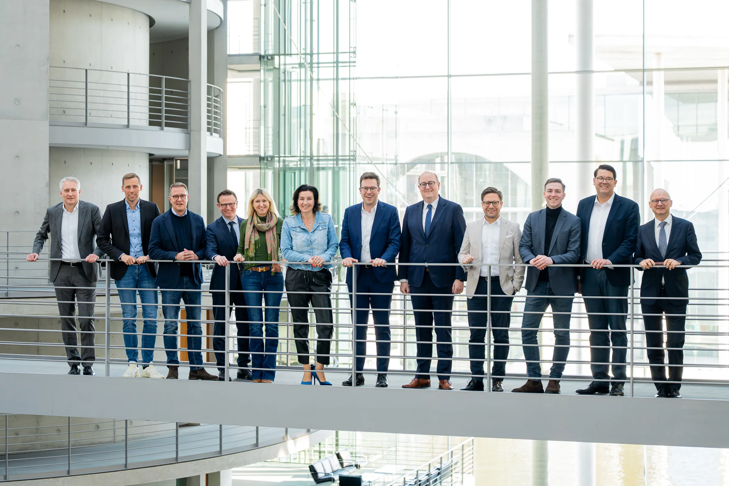 Adrian Grasse steht zusammen mit Kolleginnen und Kollegen der CDU/CSU-Bundestagsfraktion lächelnd an einem Geländer in einem modernen Parlamentsgebäude.