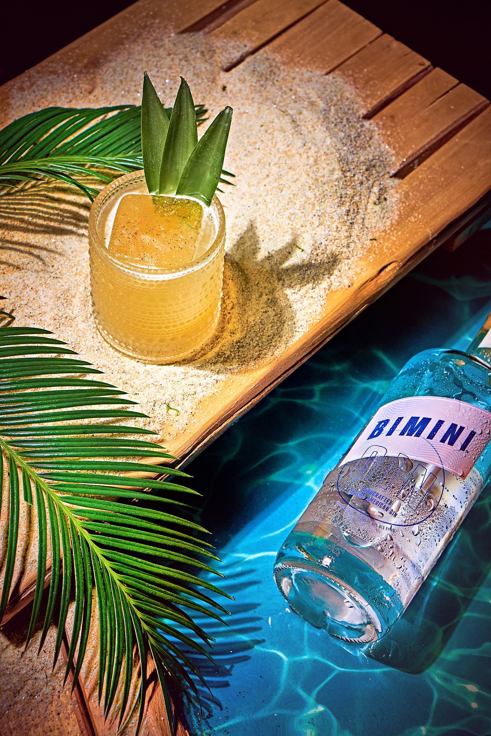 Bimini Gin bottle and cocktail beside a sunlit swimming pool