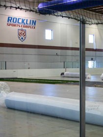 Indoor artificial turf installation at Rocklin Sports Complex with turf rolls staged on the arena floor.