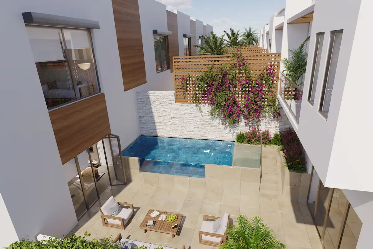 A luxurious private courtyard featuring an infinity-edge pool, a cozy outdoor seating area with wooden furniture, lush greenery, and cascading bougainvillea on a wooden lattice. The surrounding modern townhomes have large windows and folding glass doors, seamlessly blending indoor and outdoor living.