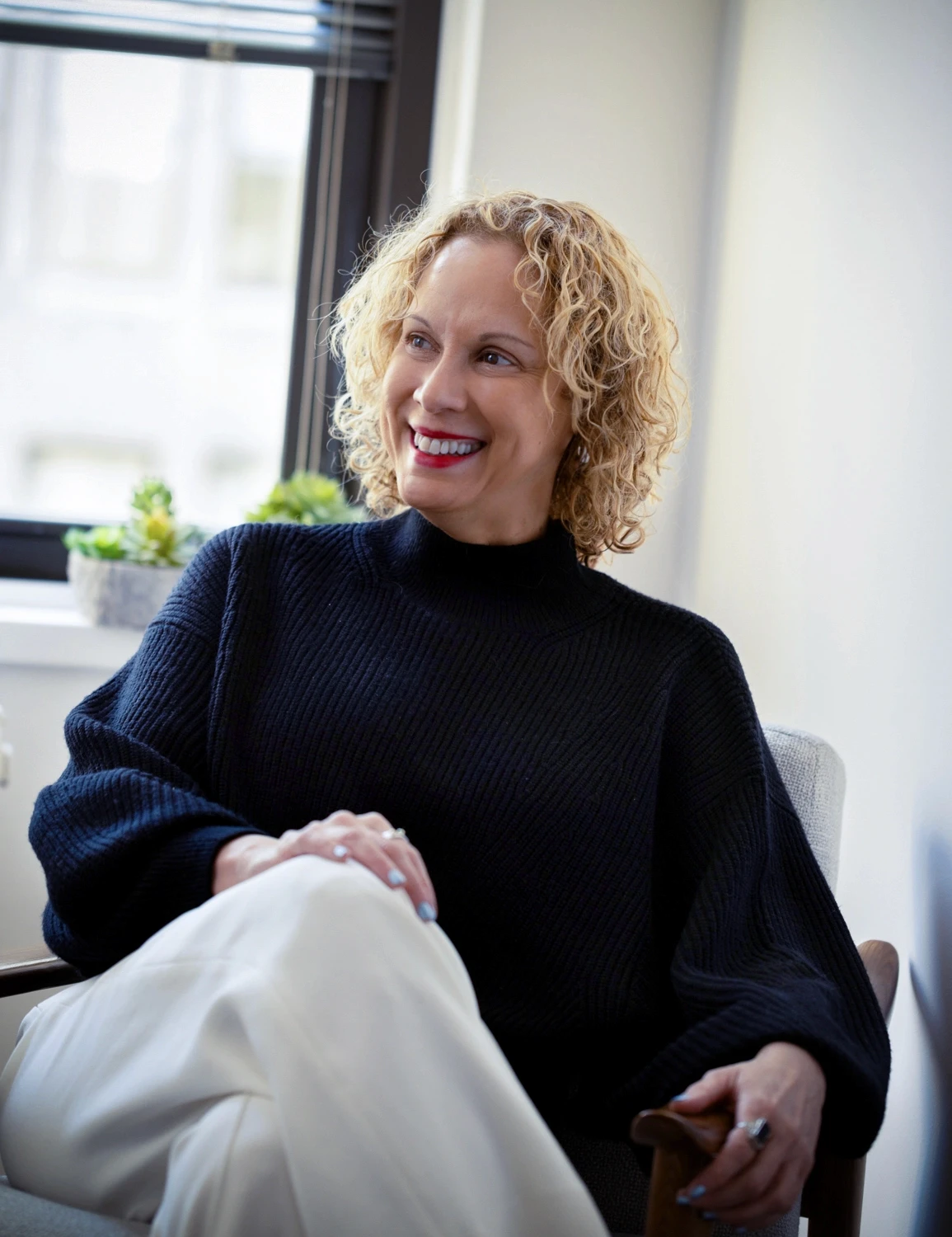 an inviting photo of a expansive therapy therapist sitting in a chair reflecting while looking out on new york city through a window representing healing and coping tools provided around anxiety therapy.
