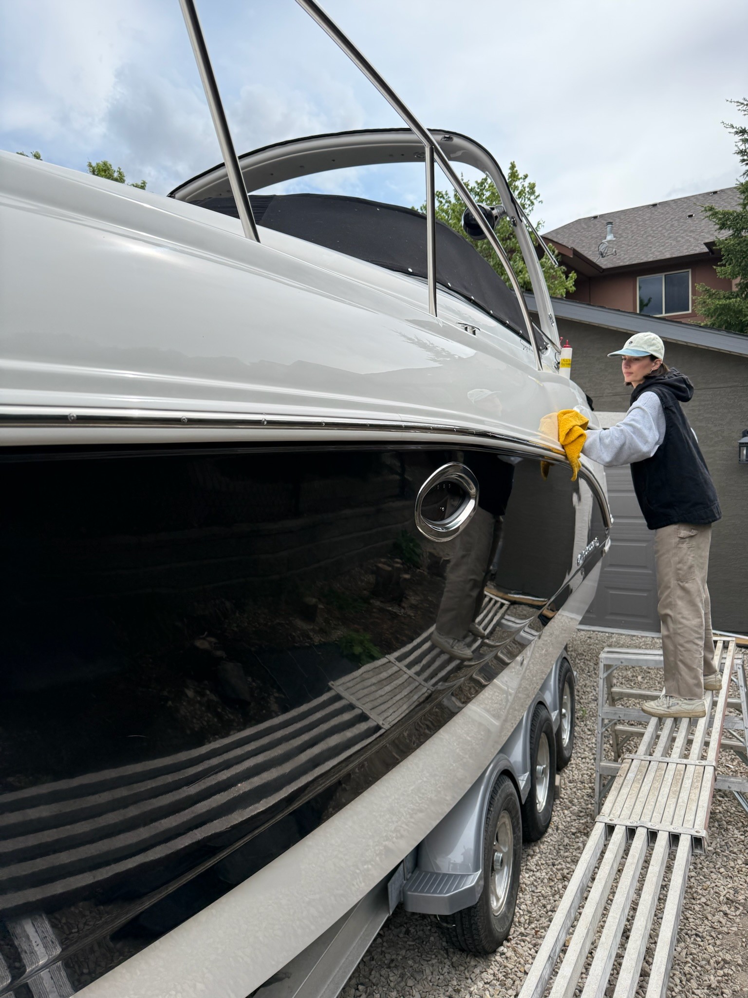 A woman standing on a plank wiping the side of a large boat with a microfiber cloth. She just performed a detail and is doing a polymer sealant