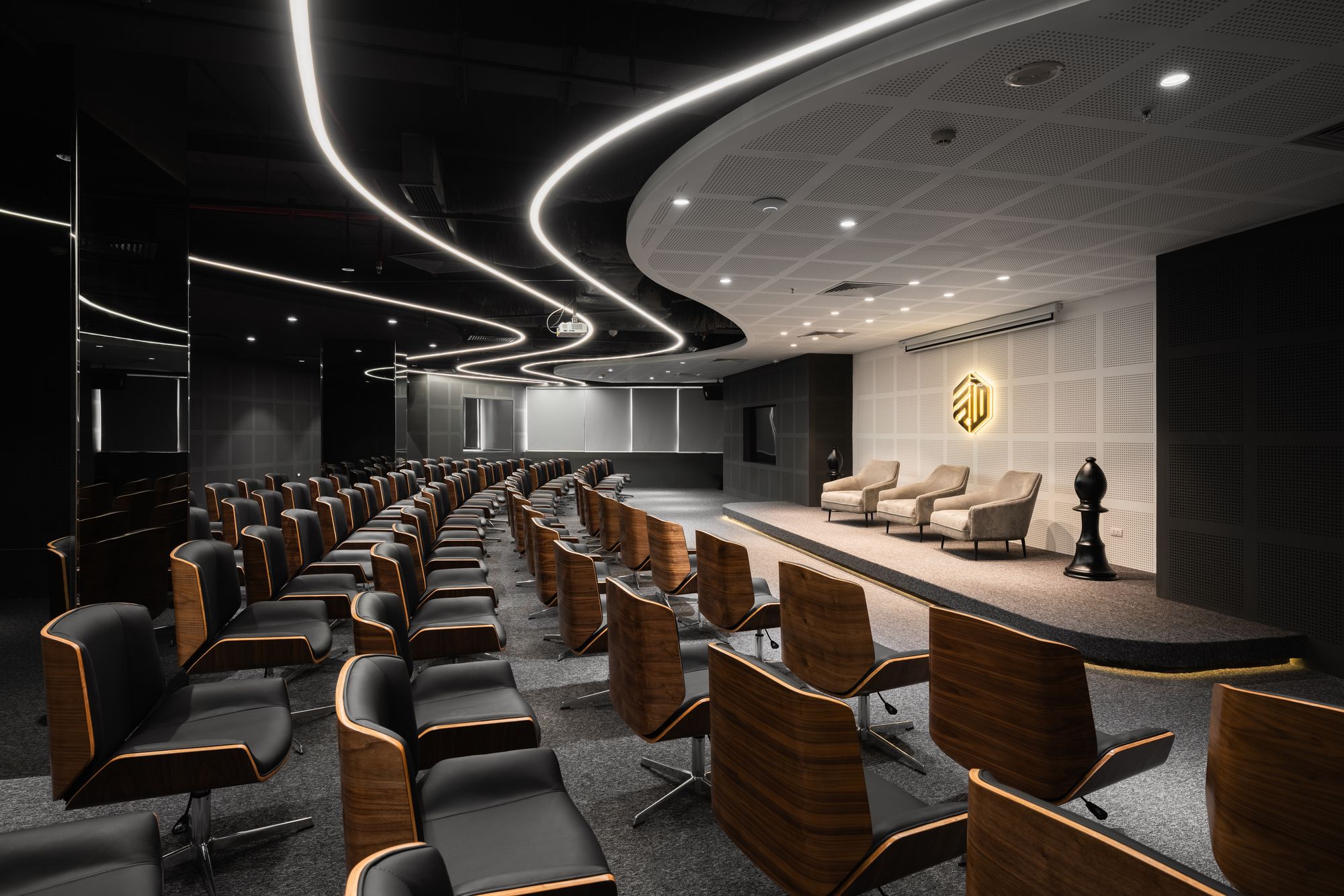 A modern conference room with curved lighting, rows of wooden chairs, and a minimalist design.