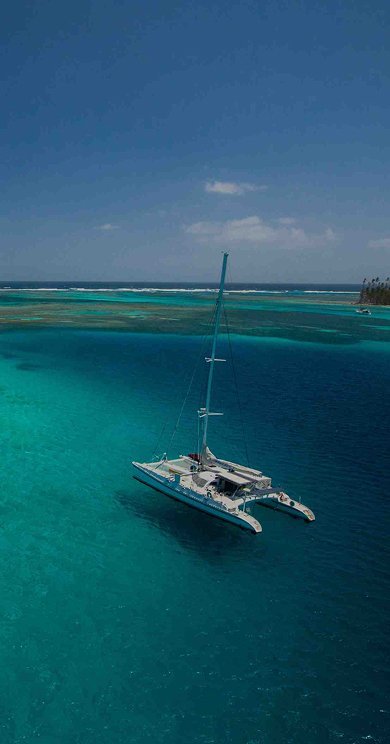 Catamaran anchored in turquoise tropical water near coral reefs and island.