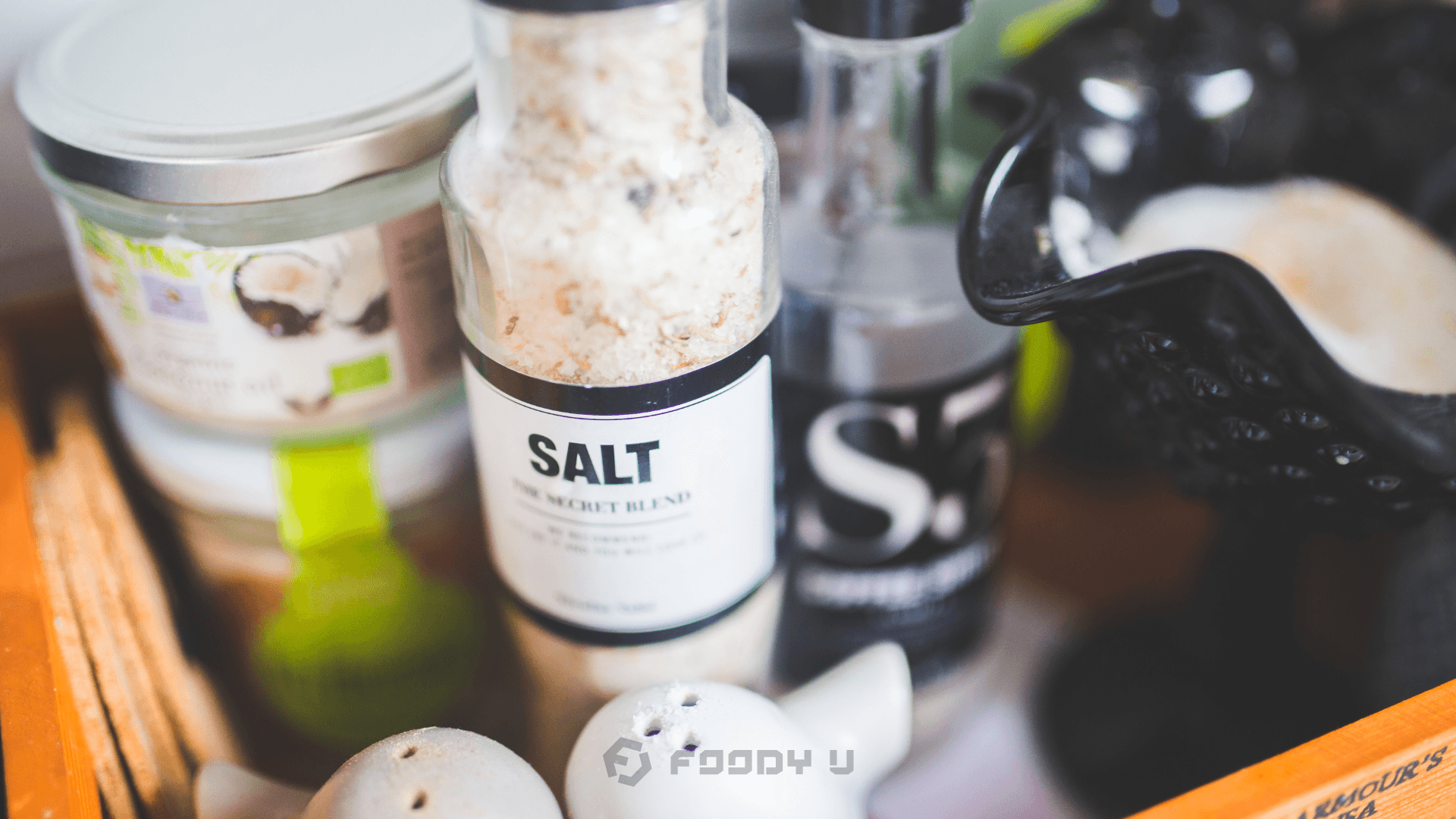 Close-up of salt grinder and seasoning jars with Foody U logo — article about sodium, salt intake, and health effects