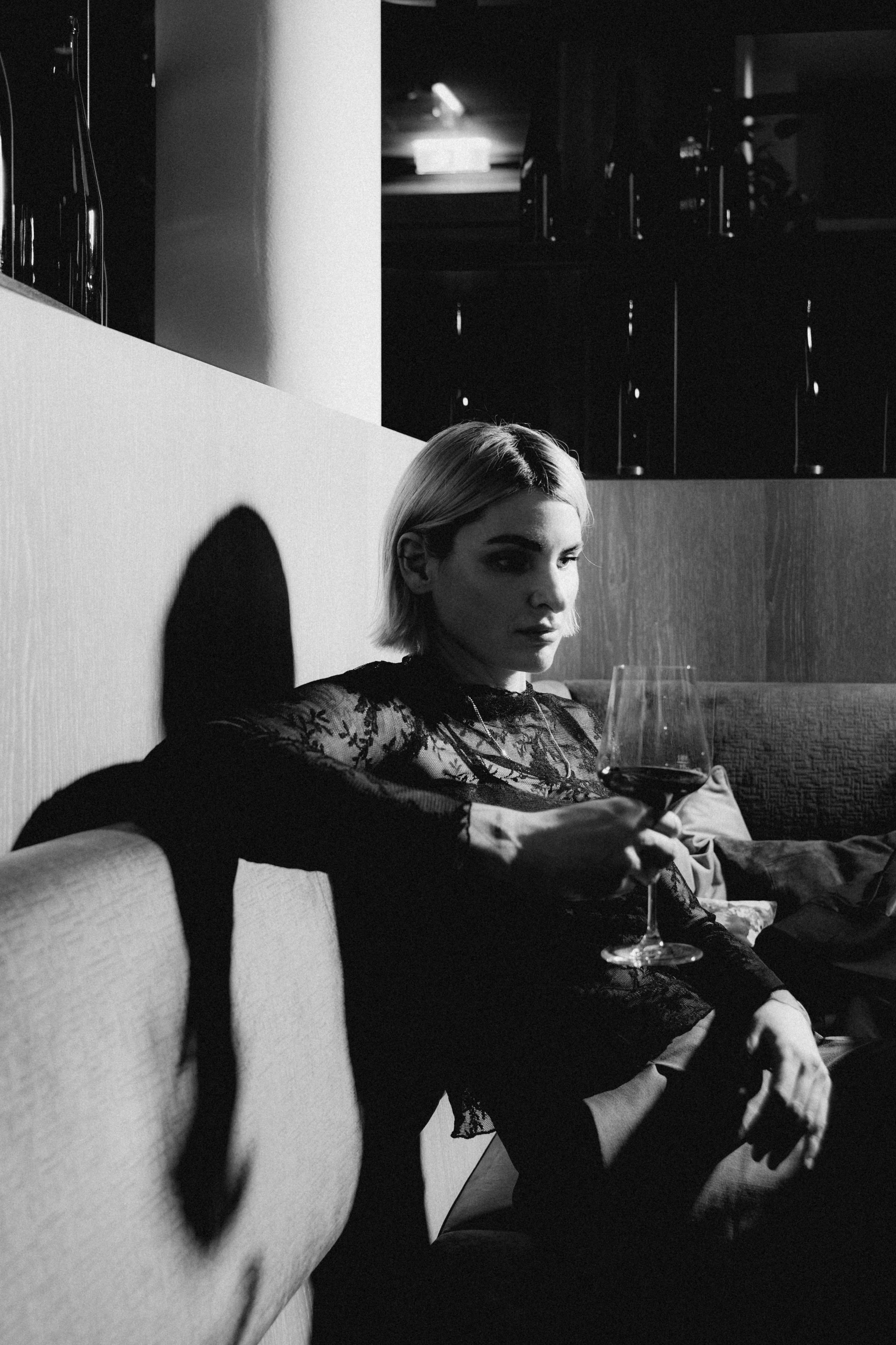 Black and white image of a person sitting against a wall, with dramatic shadows and soft lighting around them.