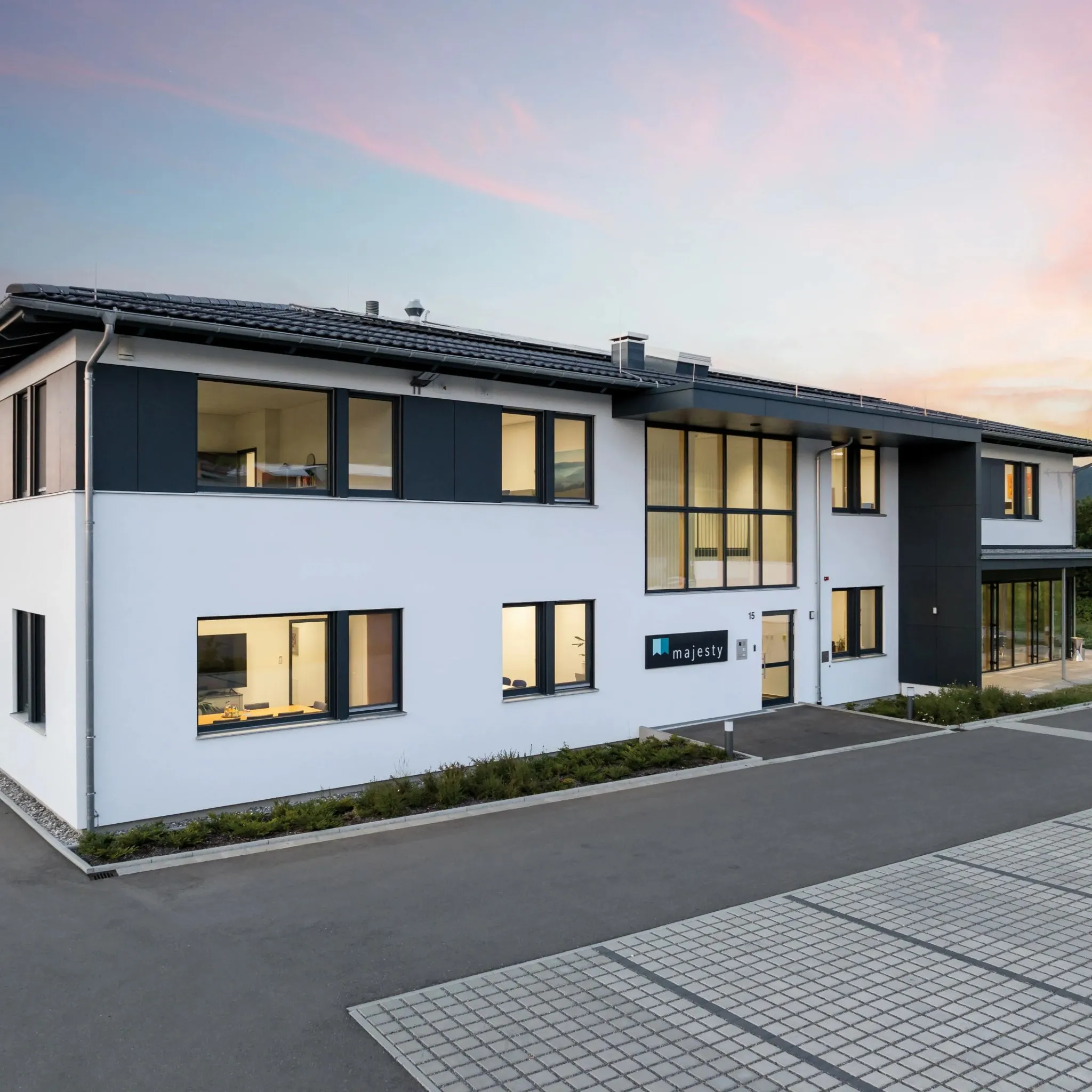 Modernes Bürogebäude 'Majesty' mit weißer Fassade, großen Fensterfronten und grau abgesetzten Elementen bei Dämmerung.