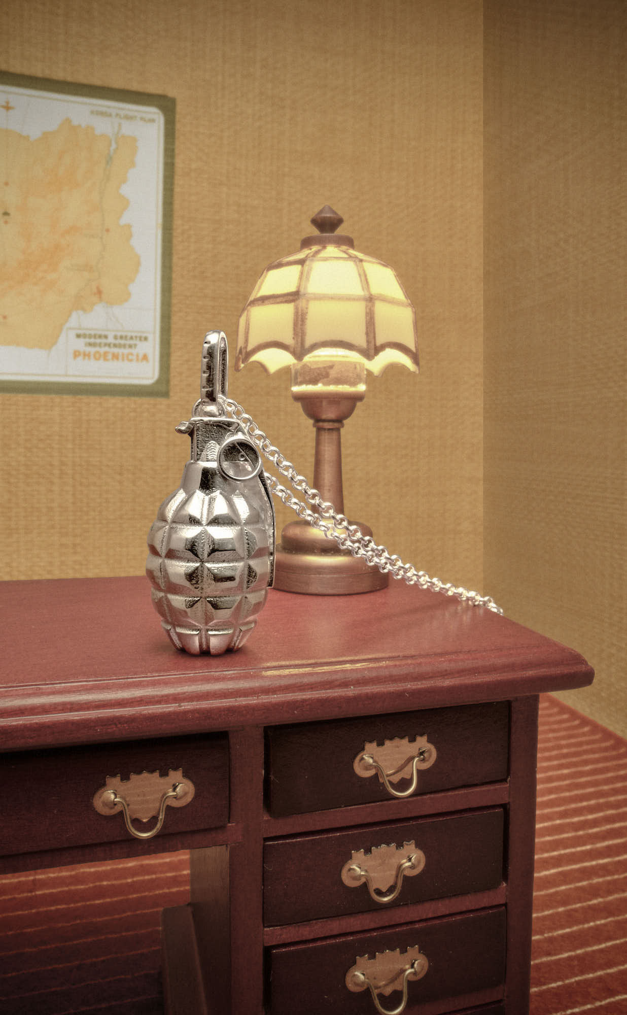 Silver grenade pendant on a wooden desk with vintage lamp and map background.