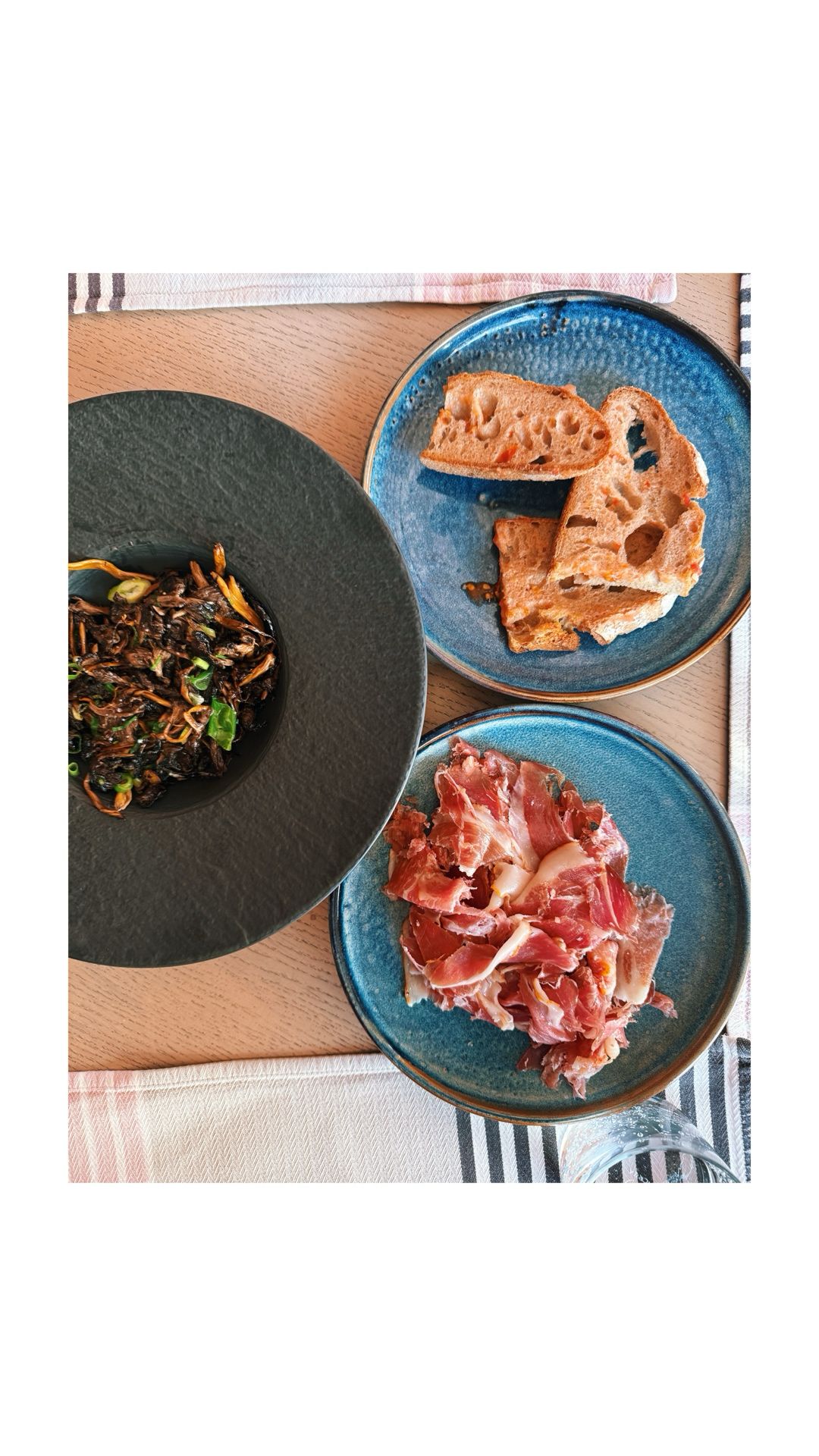 A group of friends enjoys a picnic lunch under a large pine tree in a scenic mountain valley.
