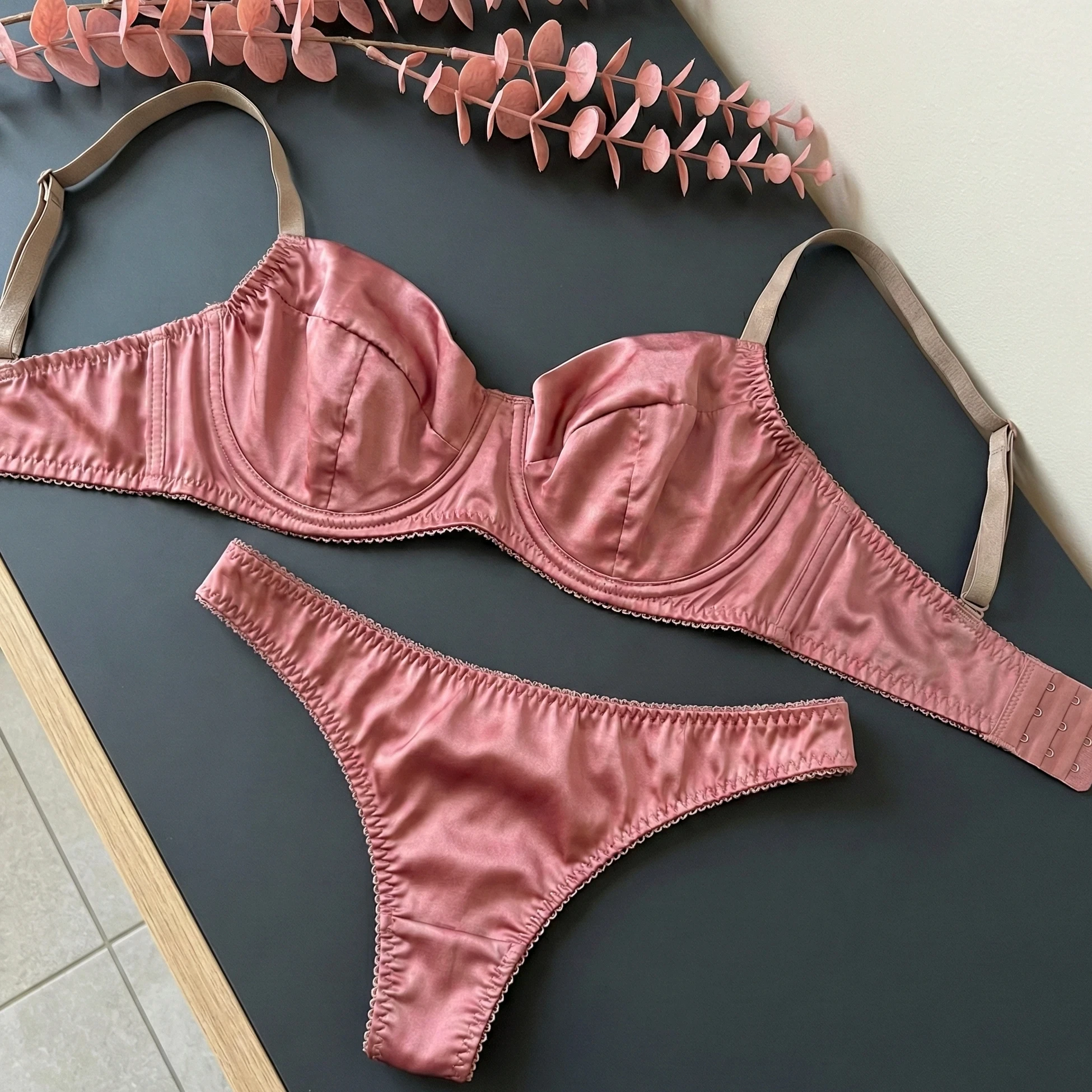 Pink satin bra and briefs arranged flat on a dark tabletop.