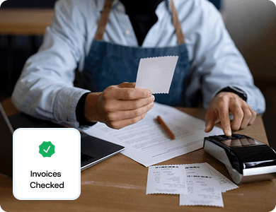 Business professional checking invoices at a desk with a digital badge reading “Invoices Checked,” representing automated invoice validation.