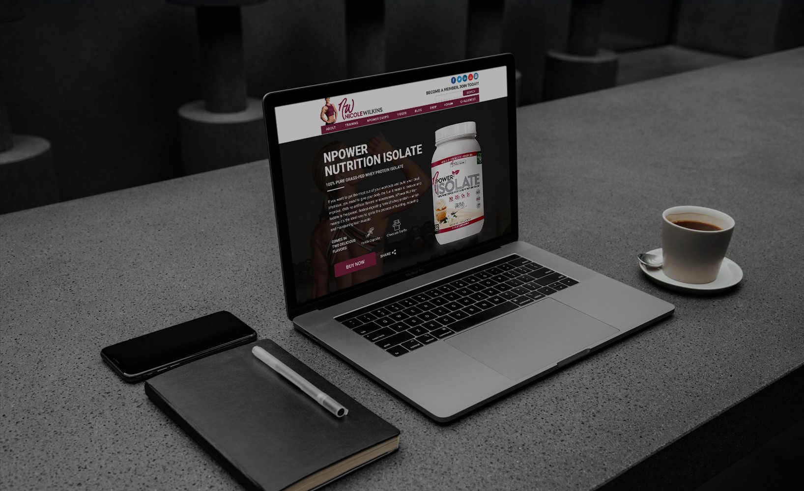 Laptop on table displaying Nicole Wilkins fitness website with NPower Nutrition Isolate product page open, beside notebook and coffee cup.