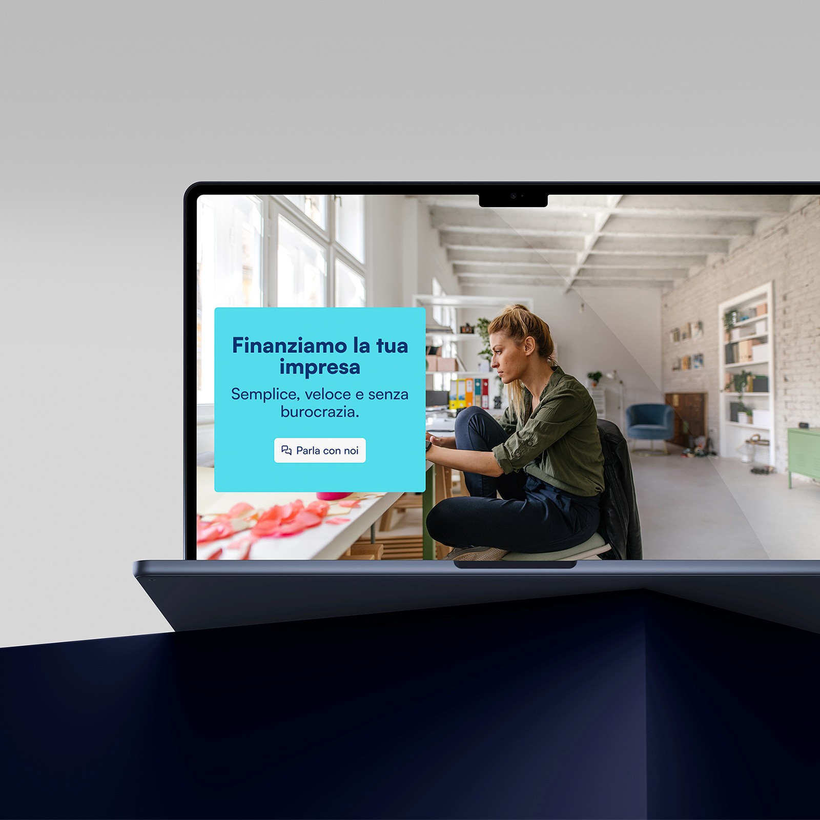 A laptop on a dark surface showing a woman working in a bright home office. On the screen is a Finpromoter message in Italian: “Finanziamo la tua impresa” (We finance your business). Below it reads “Semplice, veloce e senza burocrazia” (Simple, fast, and without bureaucracy), followed by a button labeled “Parla con noi” (Talk to us).