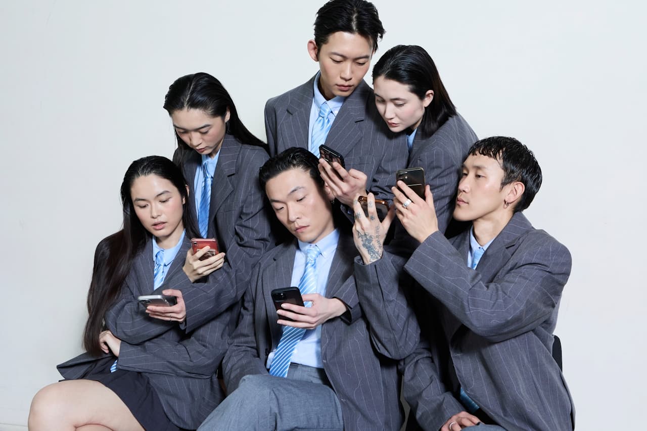 A group of men and women looking at their phones, wearing suits and ties.
