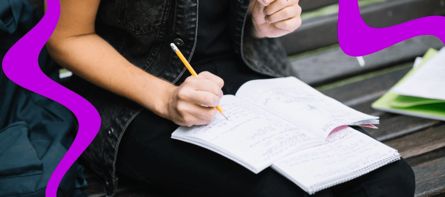 High school student planning and writing a research paper at a desk with notes and a laptop