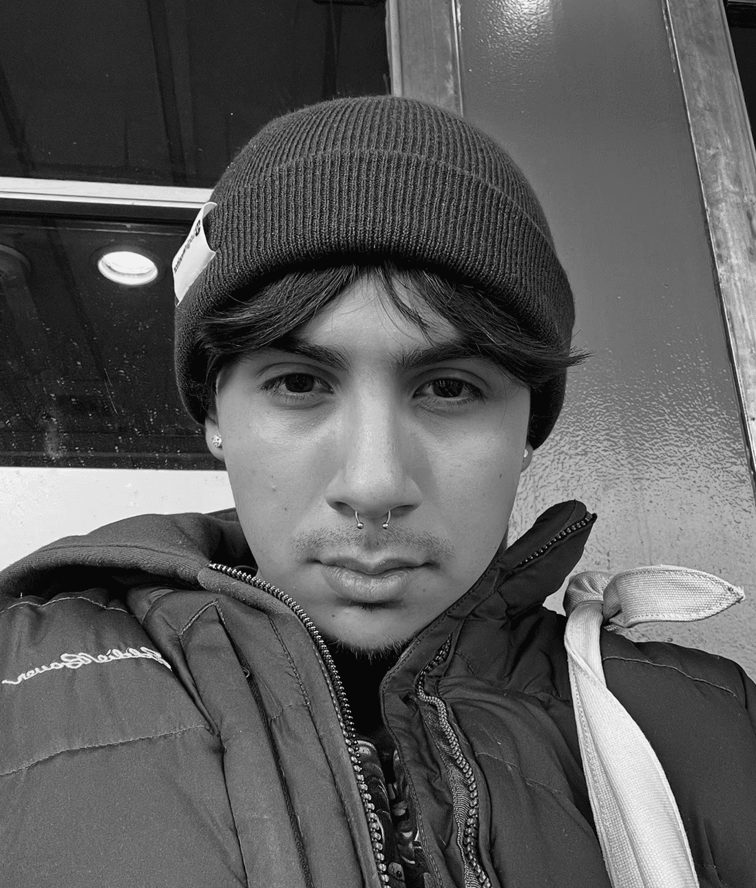 A thoughtful young person with dark hair gazes to the side, captured in soft black and white lighting.
