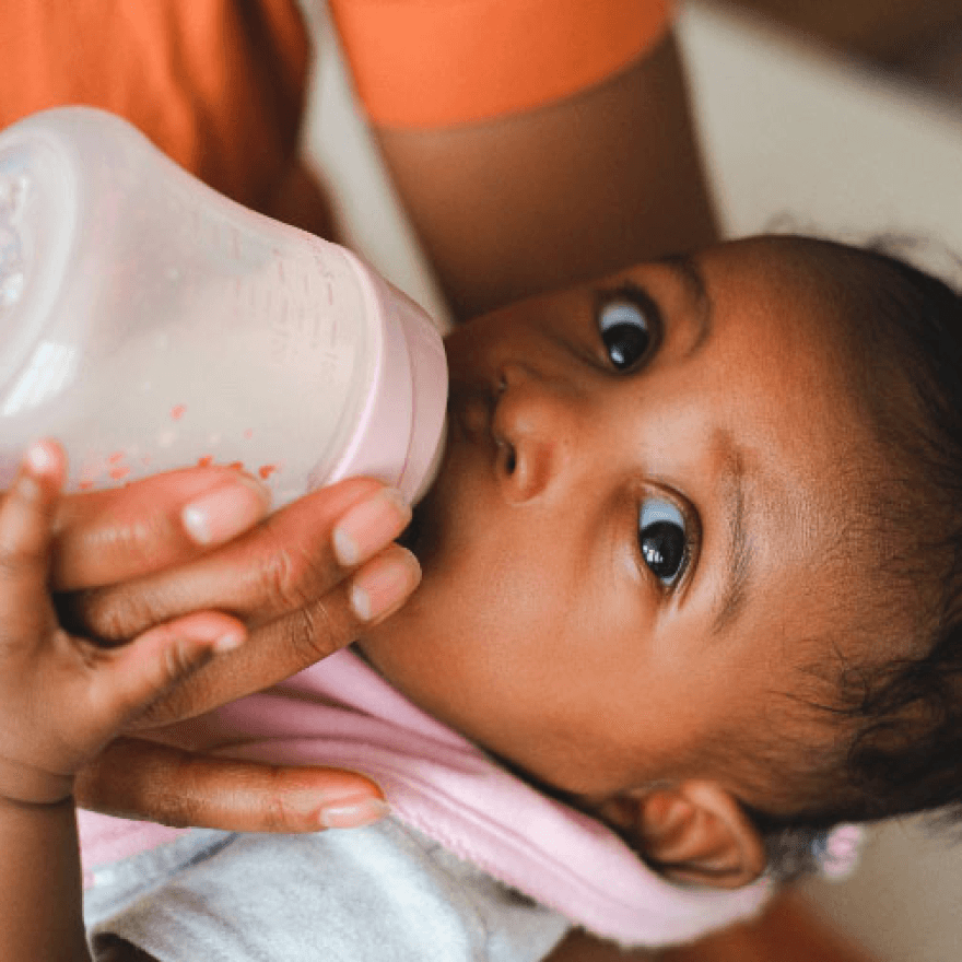 A woman gently feeds a baby with a bottle.