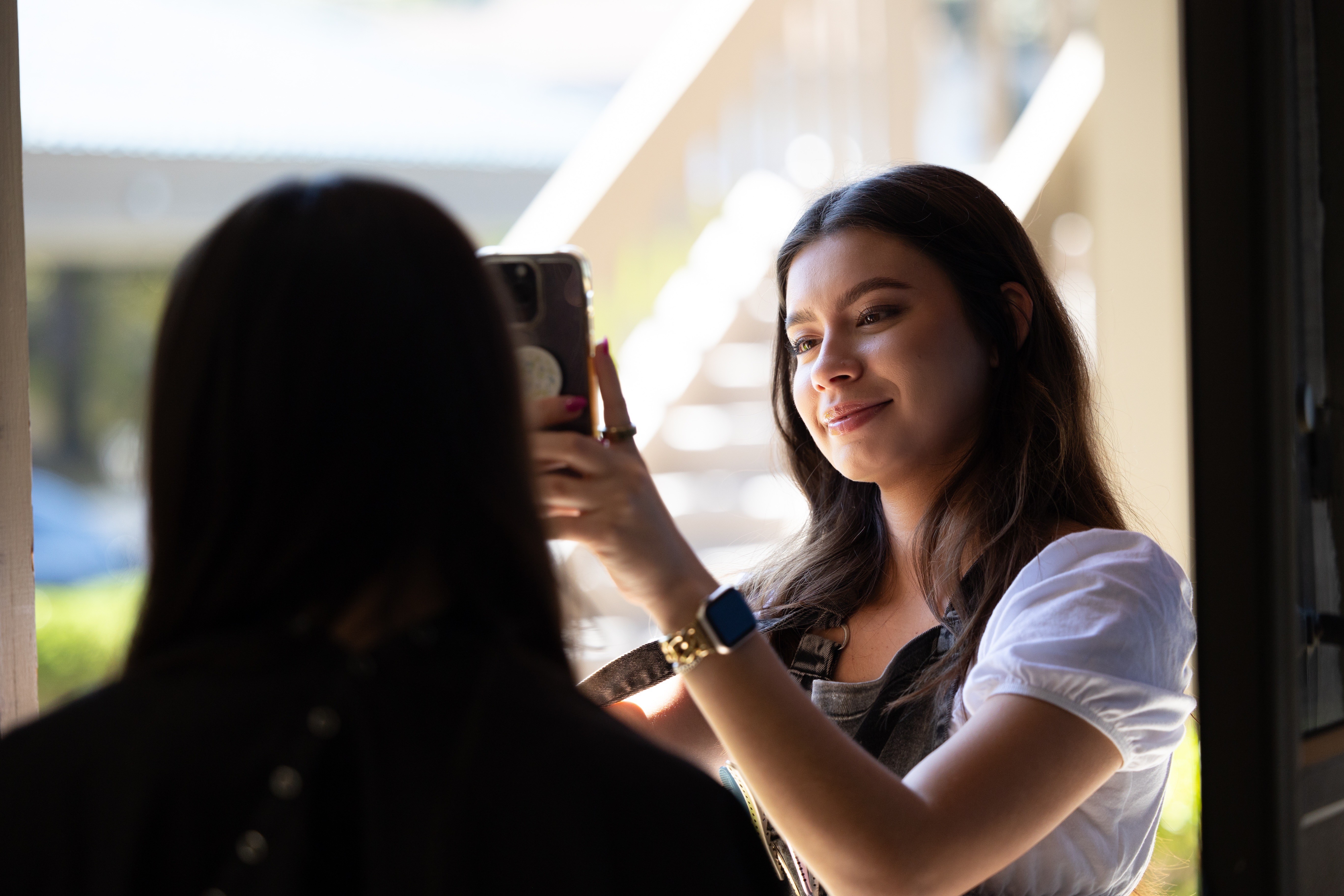 a woman taking a pircture smiling of another woment with her back to the photo