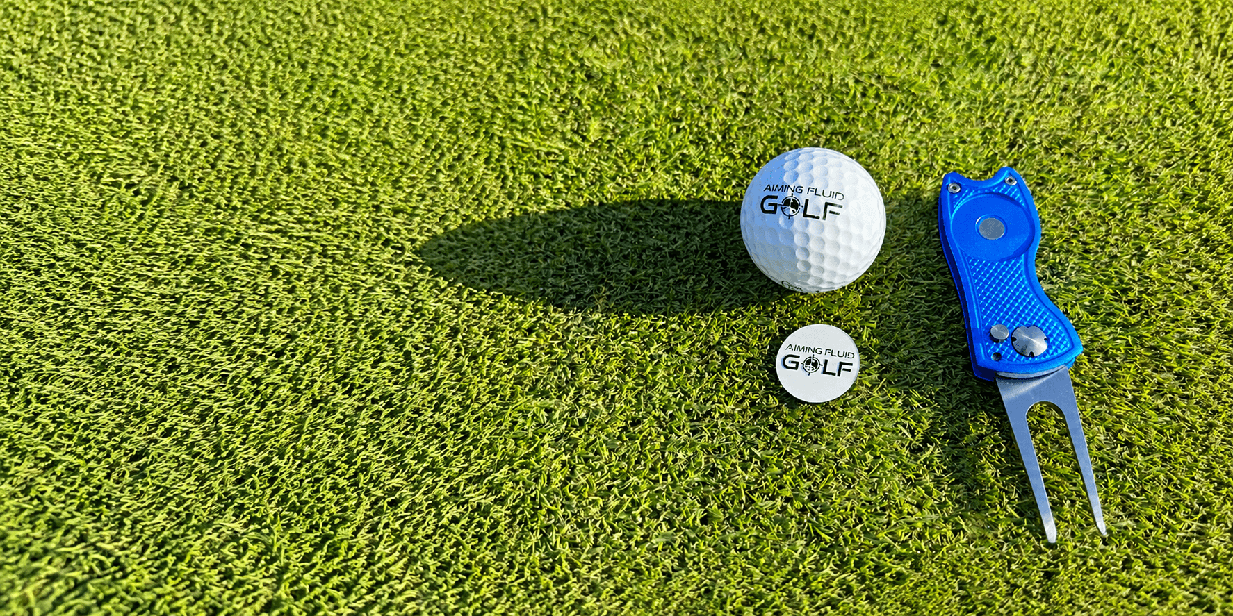 Aiming Fluid Golf ball marker, golf ball, and divot tool displayed on a putting green.