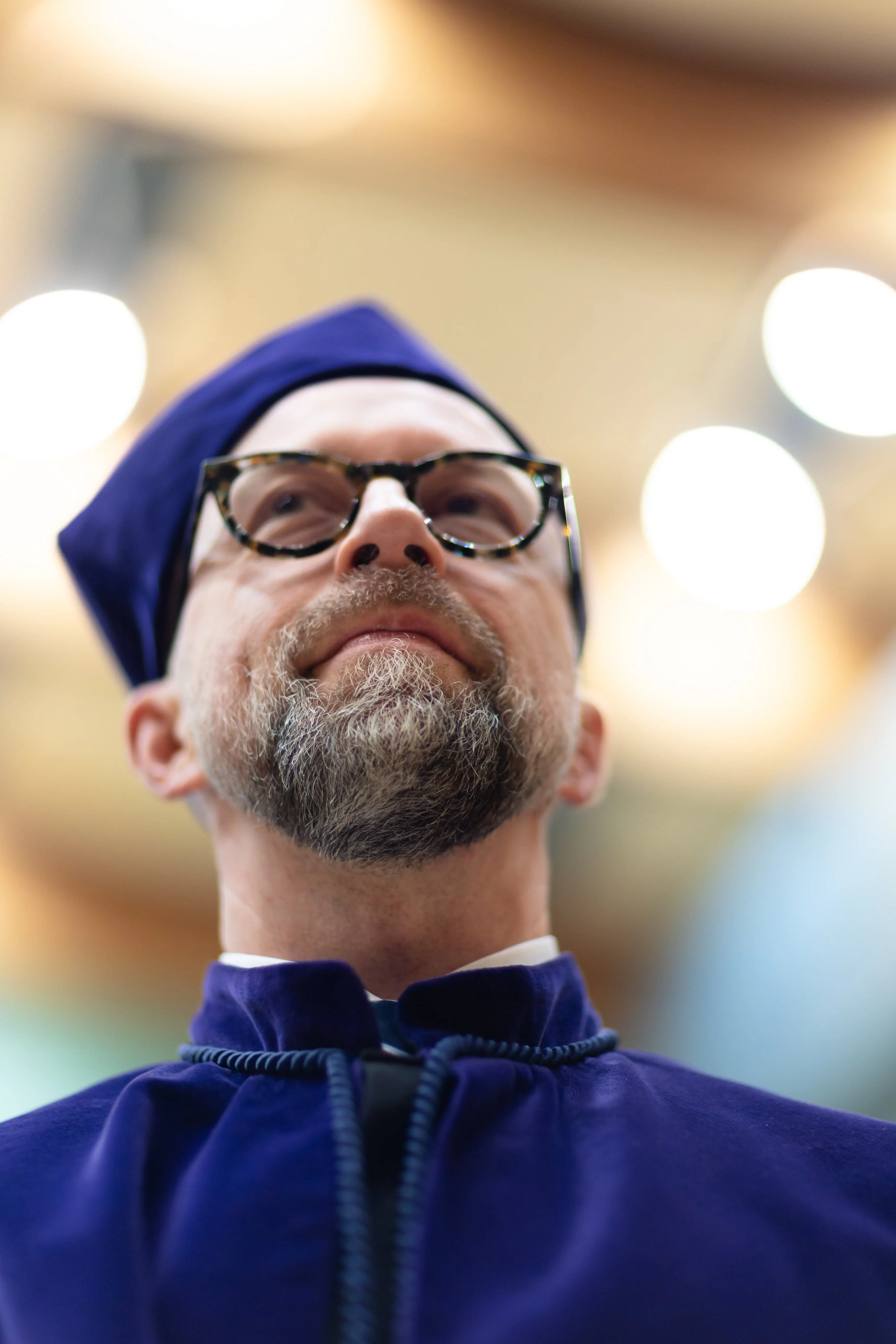 Portret mężczyzny w średnim wieku ubranego w togę rektorską. Spogląda od w górę, tło zdjęcia jest zamazane.