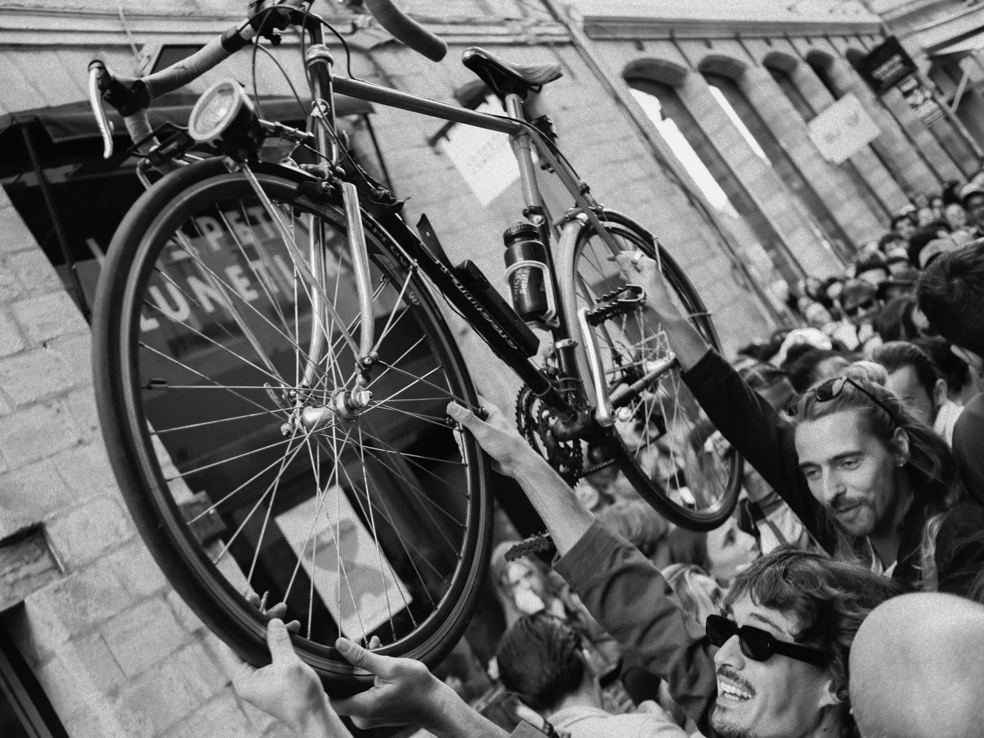 Bicycle held up above a crowd at a street market, in black and white