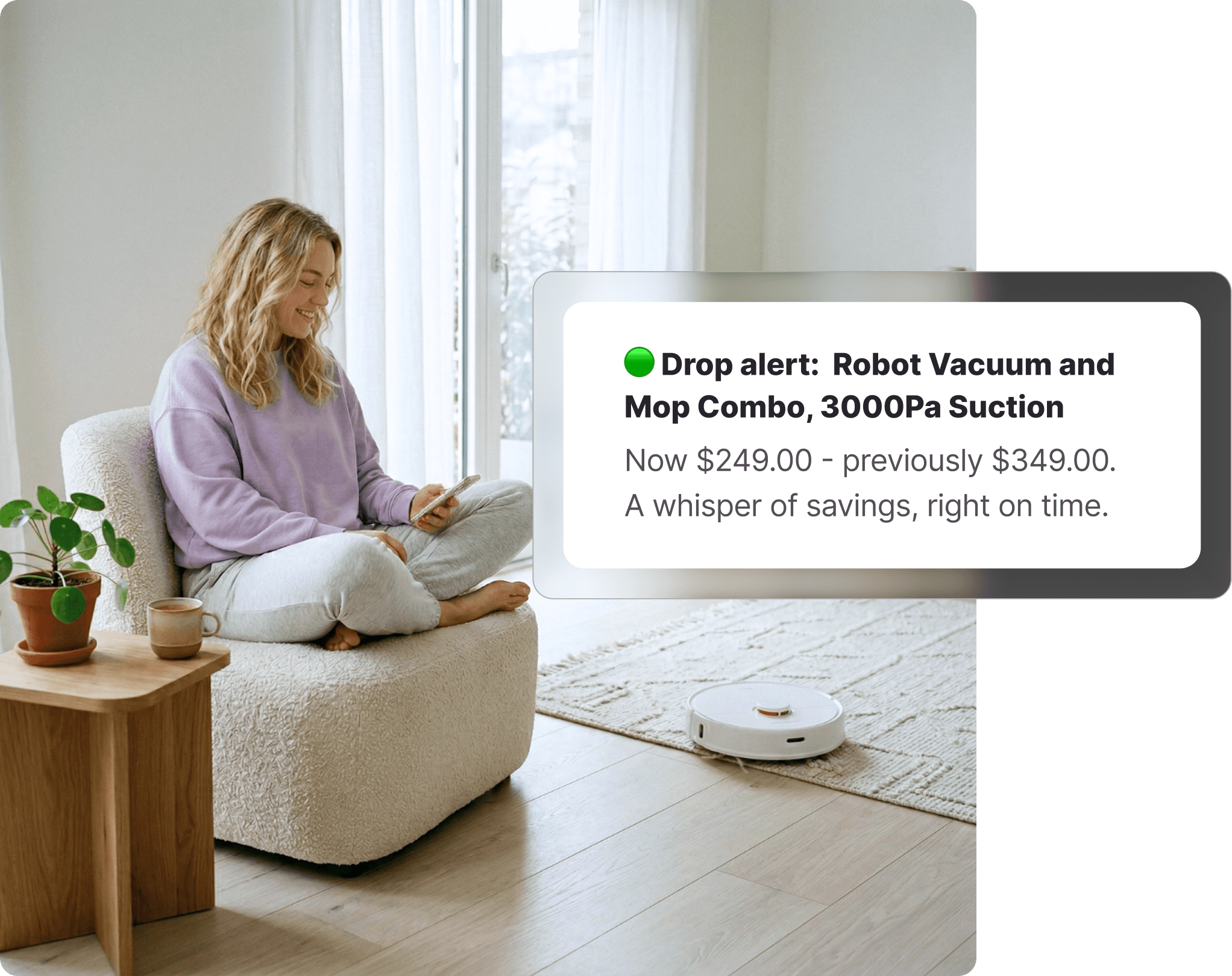 Woman sitting cross-legged on a cream armchair checking her phone, with a white robot vacuum running across the floor behind her, receiving a Kogan price drop alert.