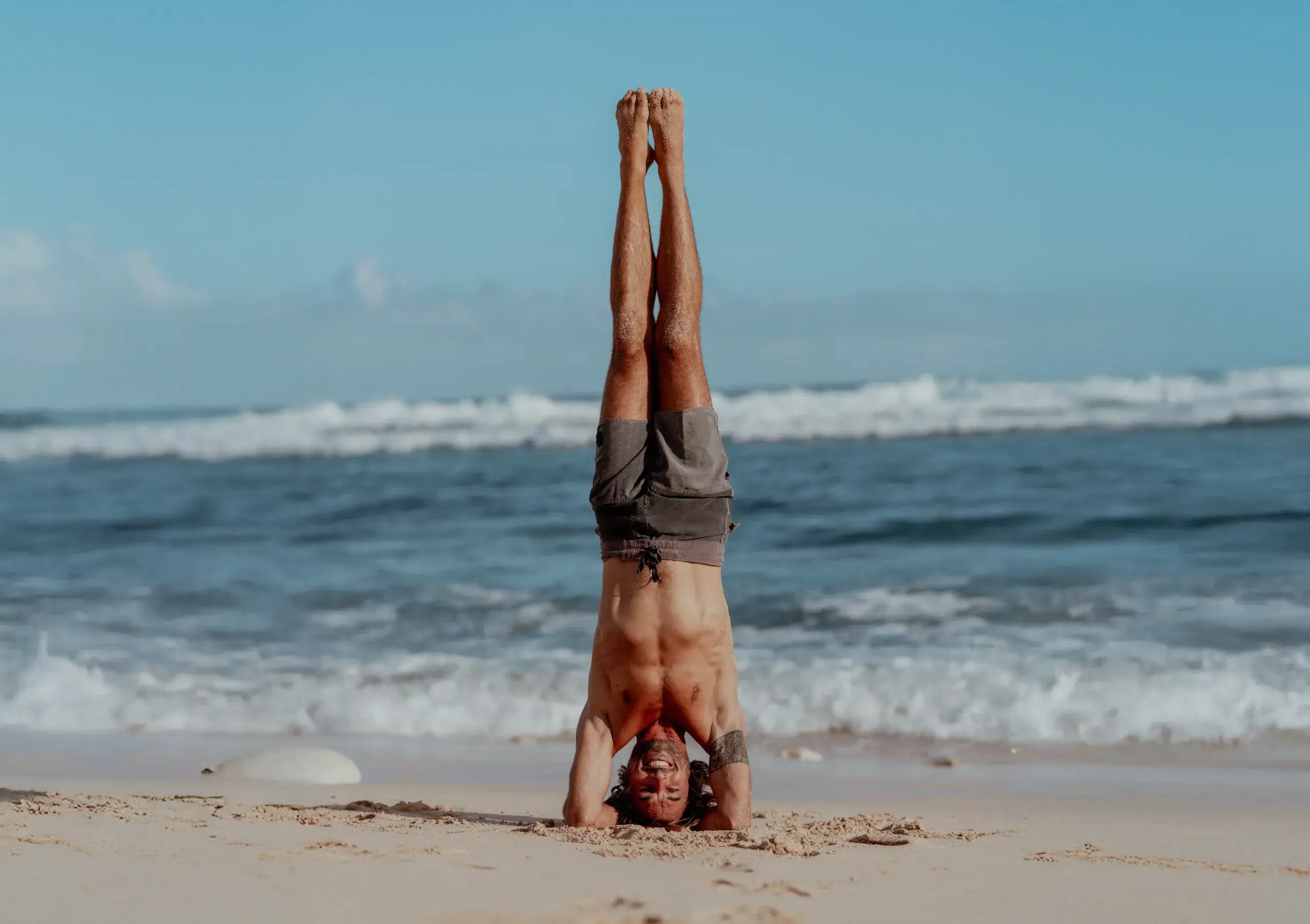 Male practitioner mastering headstand Sirsasana inversion on the beach during the 300-hour multi-style yoga training