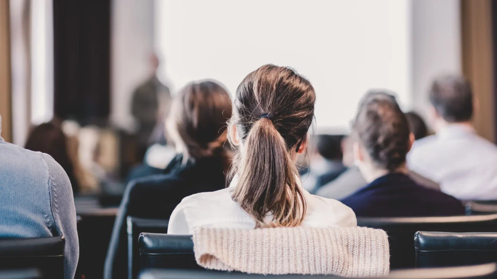 a photo of a lady in a simposium/training session, with her hair in a pony tail and wearing a white shirt