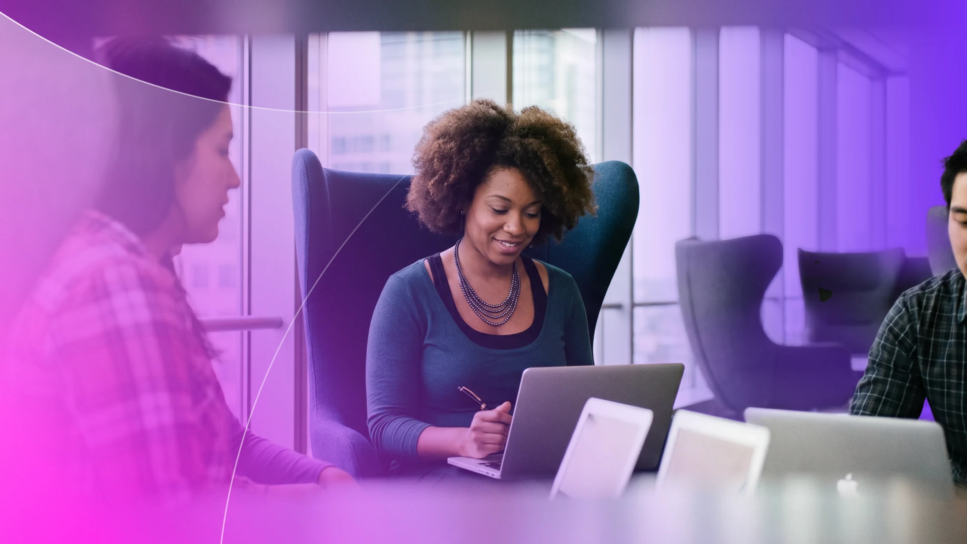 A small team of diverse professionals collaborating on laptops in a modern coworking space. The image illustrates the operational agility of SMBs and the cybersecurity challenges faced by MSPs when managing broad access rights and informal device usage in hybrid work environments.