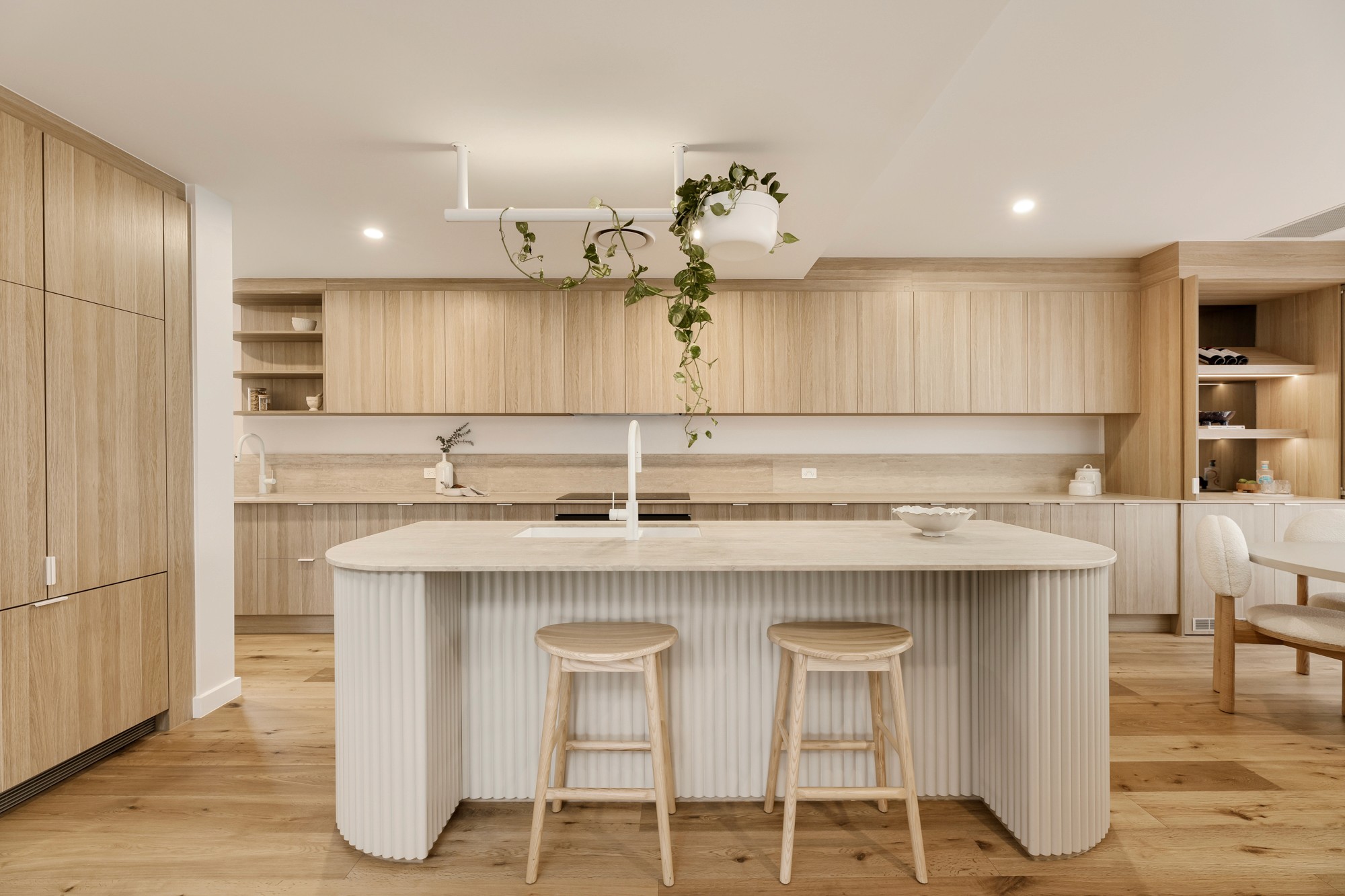 Close-up of curved kitchen island with textured timber detailing and stone benchtop.