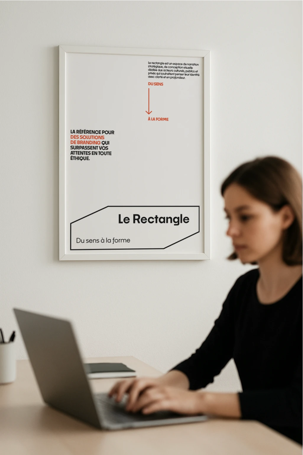 Affiche manifeste Le Rectangle version orange accrochee dans un bureau derriere une personne qui travaille sur un ordinateur.