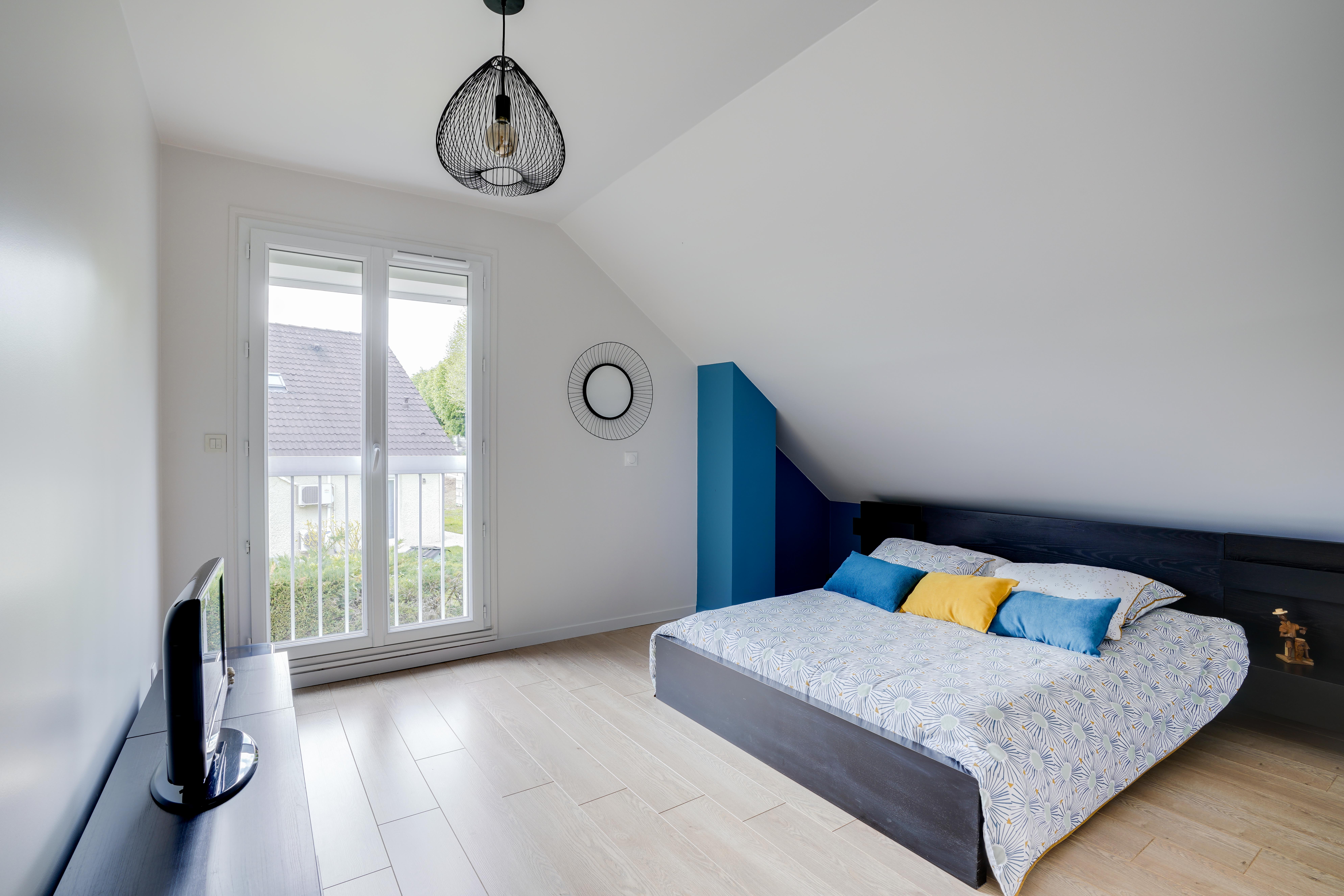 Transformation chambre 77 avec planchers bois clair, lit double bas, literie motifs et oreillers colorés, architecte d'intérieur clé en main.